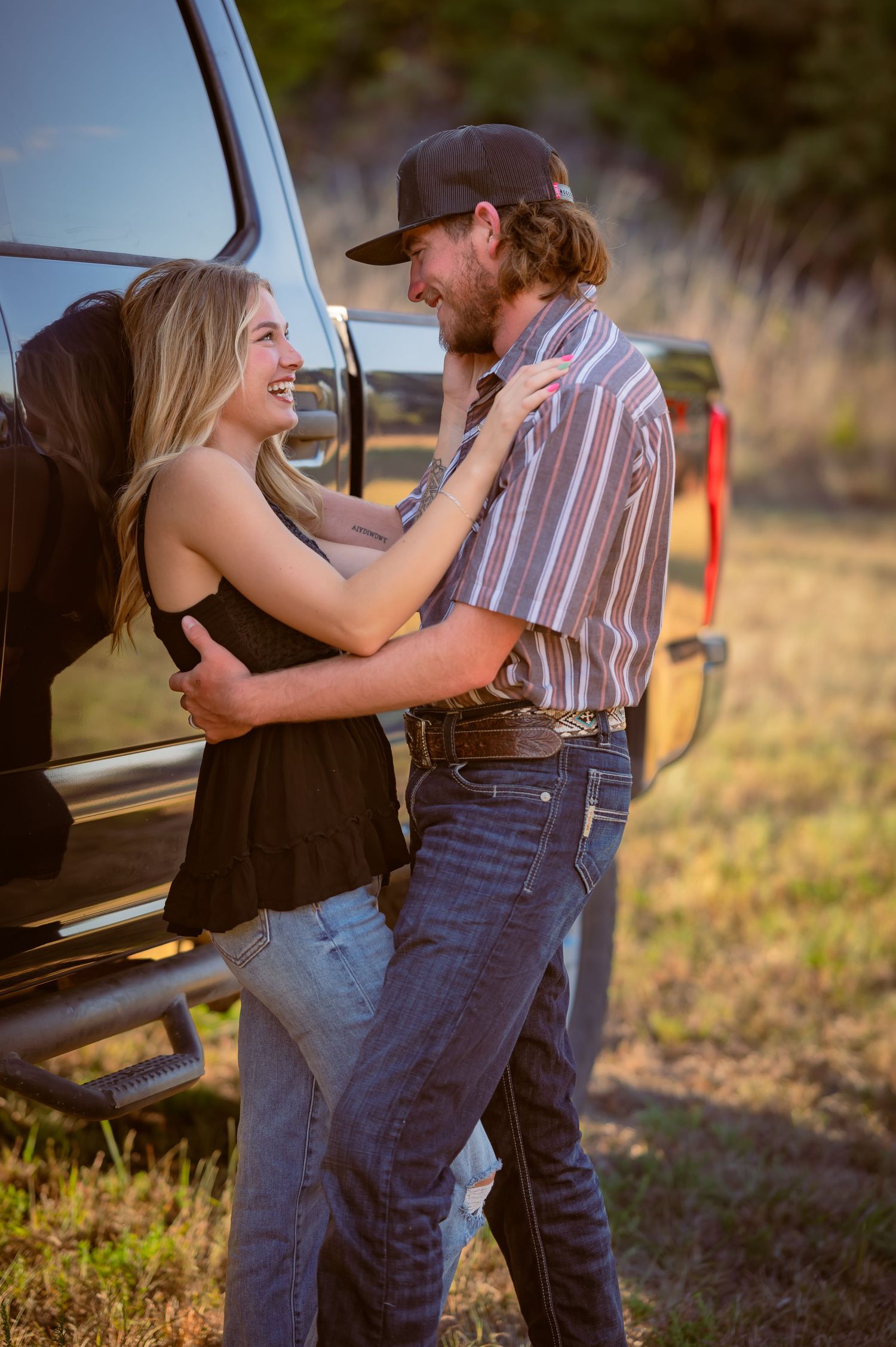Young couple embracing and laughing together beside a pickup truck in a sunny field.