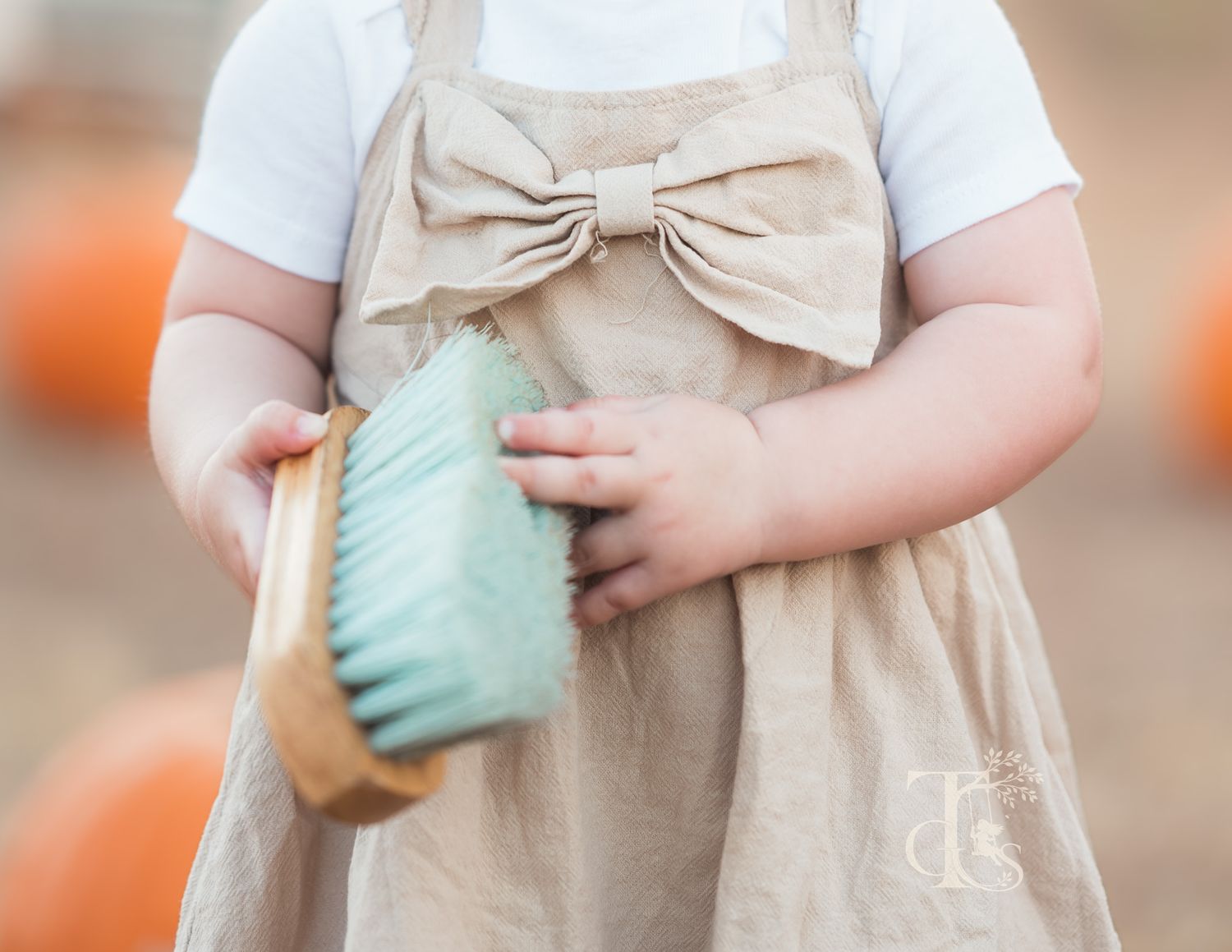 Close-up of baby in linen bow dress holding a mint green brush at a pumpkin patch.