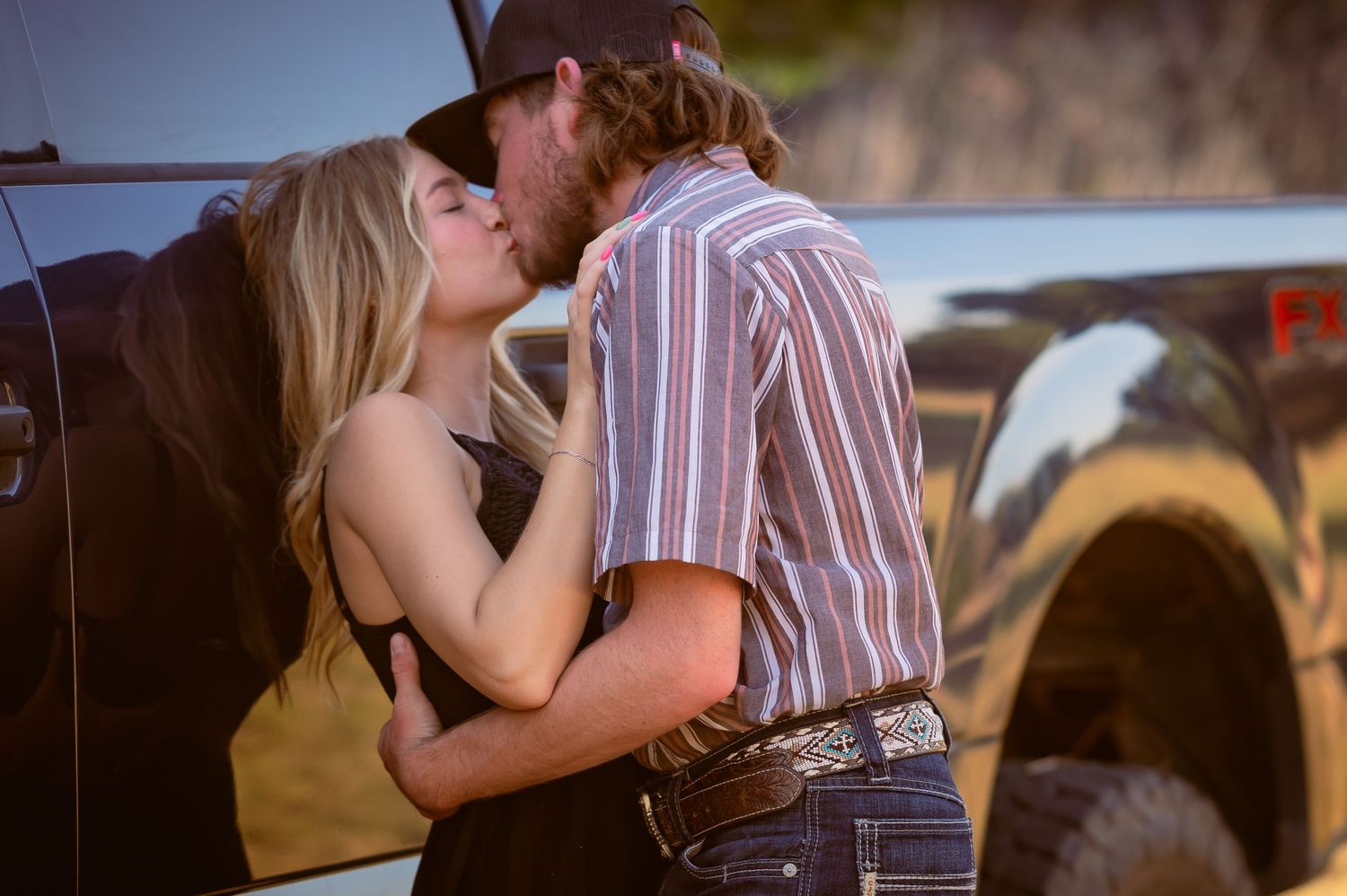 Couple sharing a passionate kiss beside a black pickup truck at sunset.