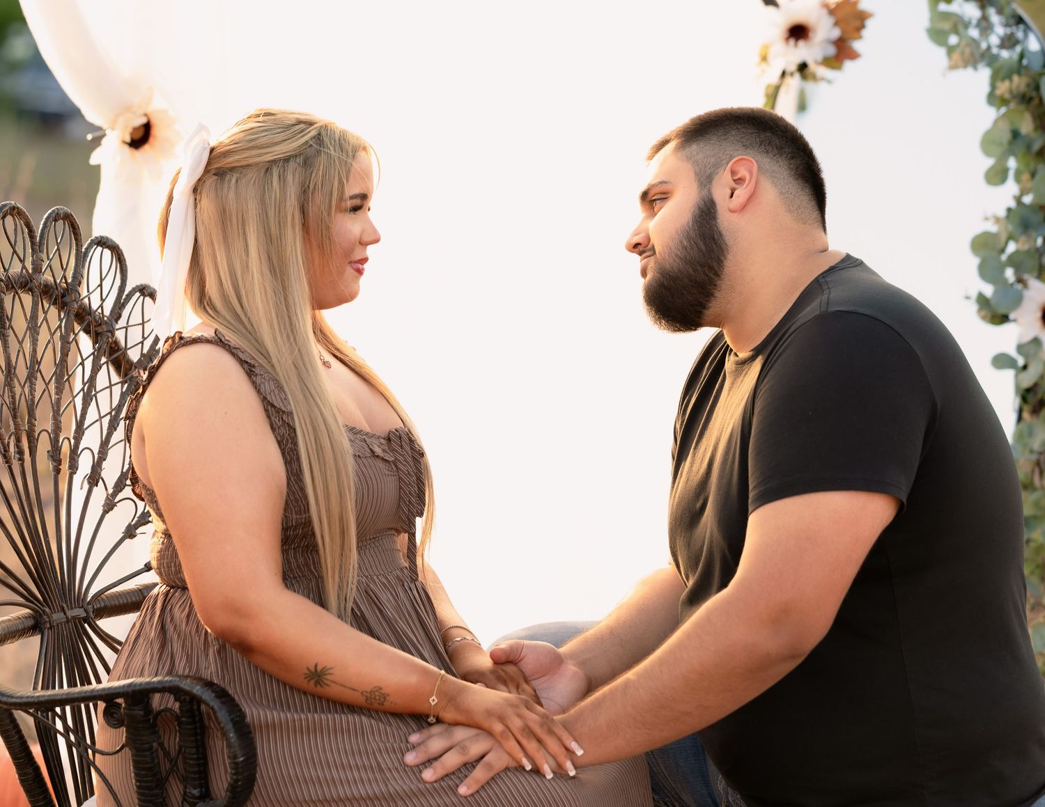 Couple holding hands and gazing at each other during an outdoor maternity photo session at sunset.