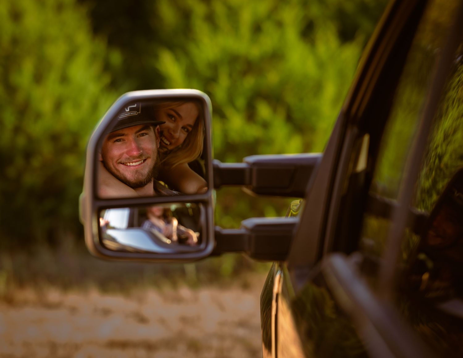 Smiling man reflected in truck side mirror during golden hour outdoor photography session.