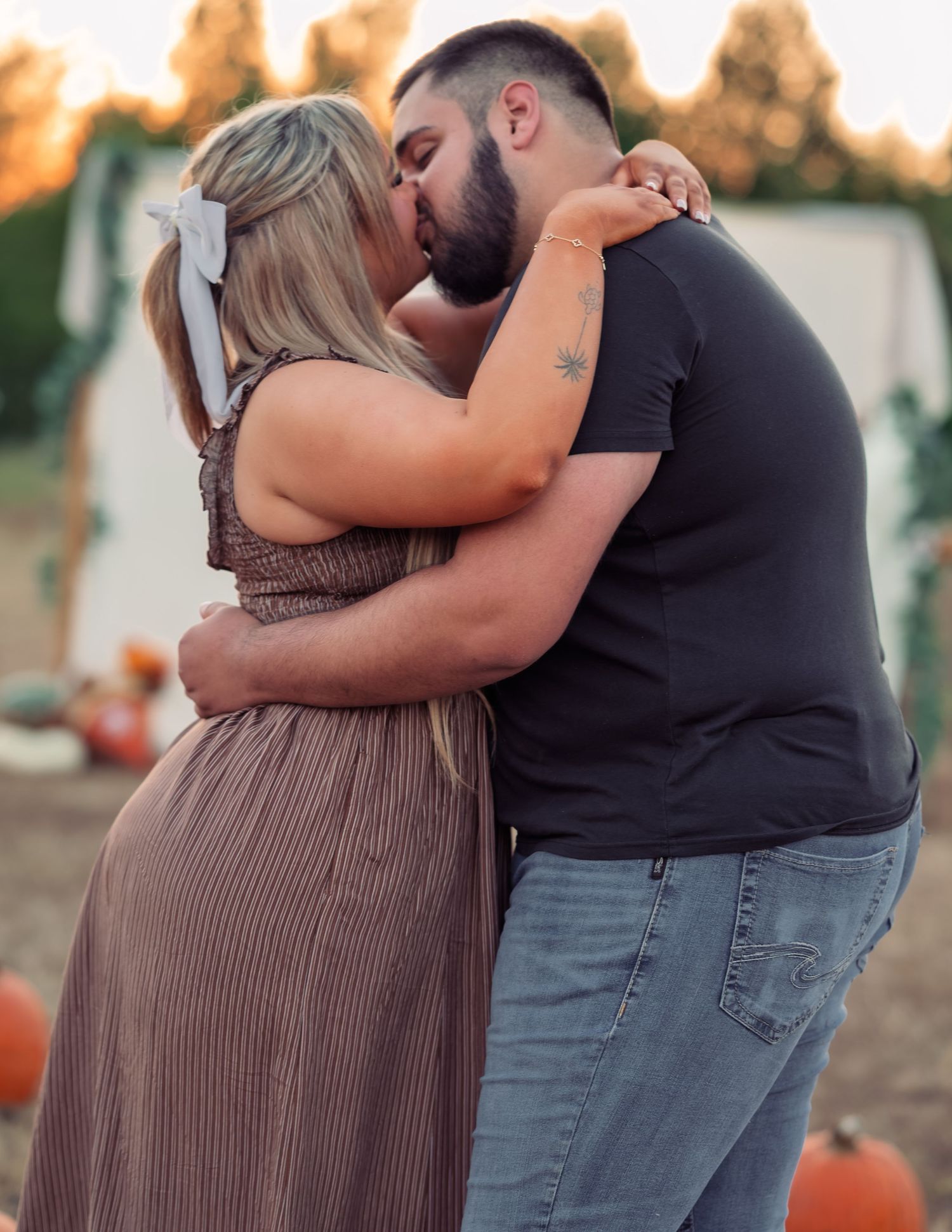 Couple sharing a romantic kiss at a pumpkin patch during golden hour sunset.