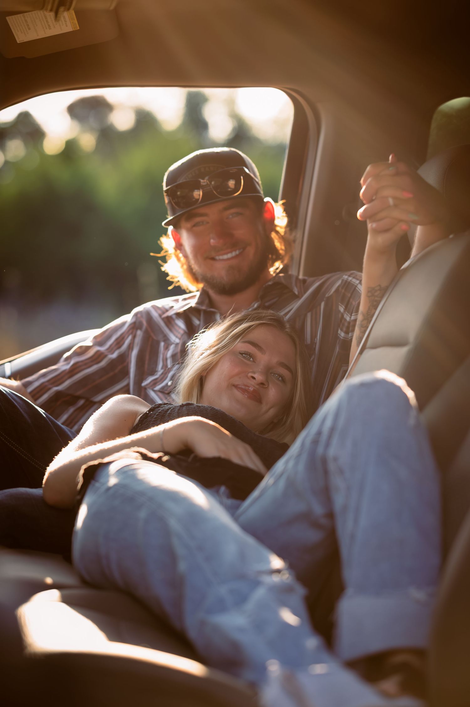 Young couple relaxing together in a truck bed, smiling in warm sunlight.