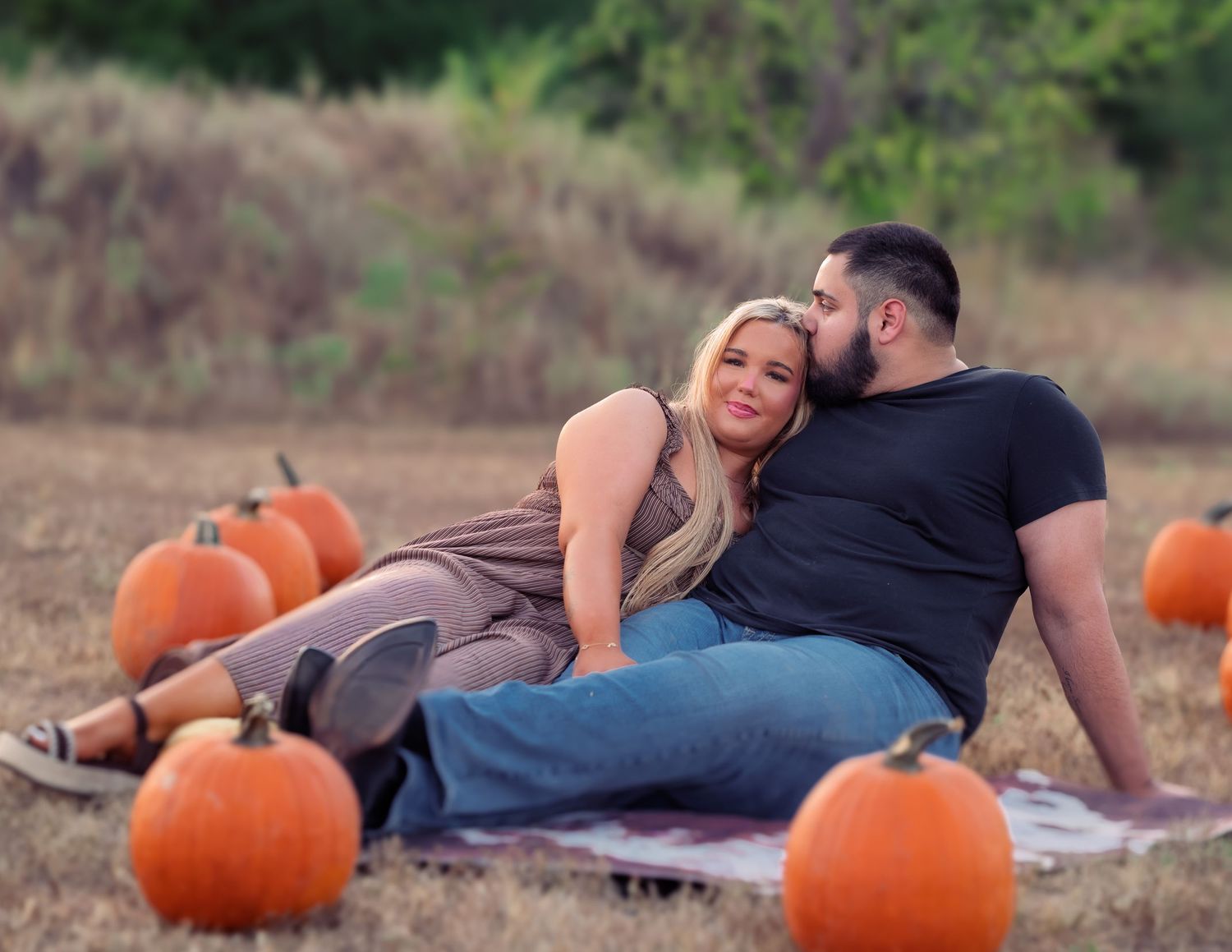 Couple relaxing on blanket in rustic pumpkin patch during warm autumn sunset engagement session.