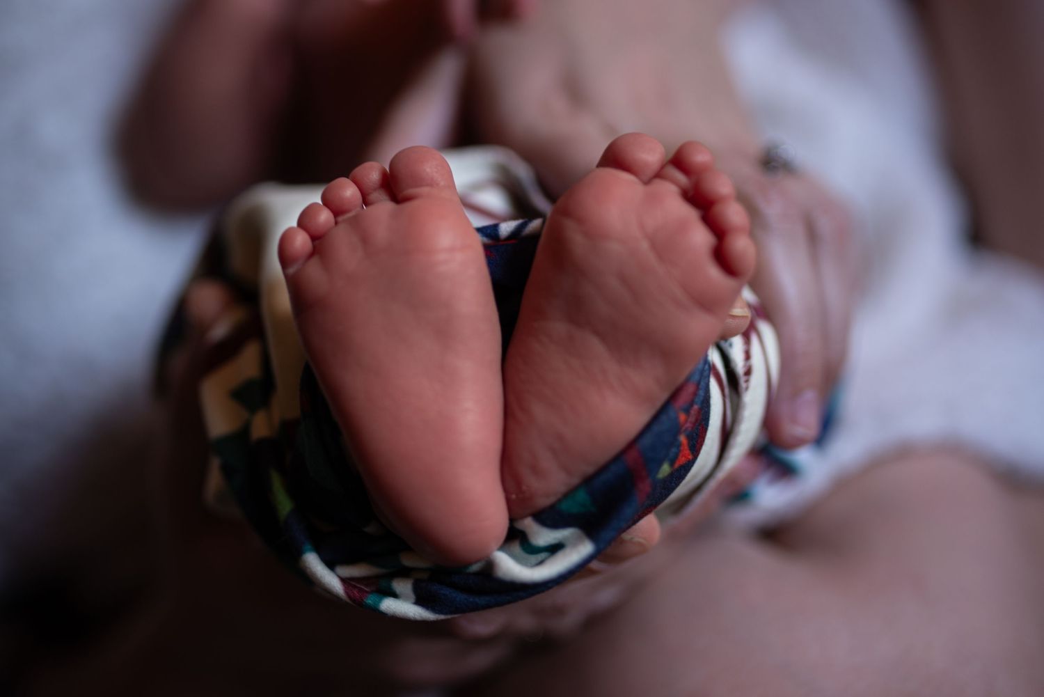 Closeup of precious newborn baby feet wrapped in colorful swaddle blanket.