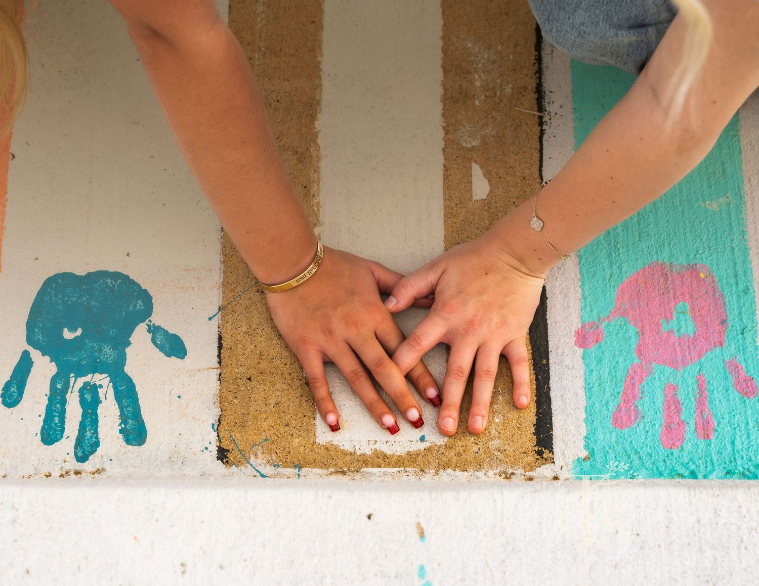 Family handprints in teal and pink paint on striped surface with hands touching together.