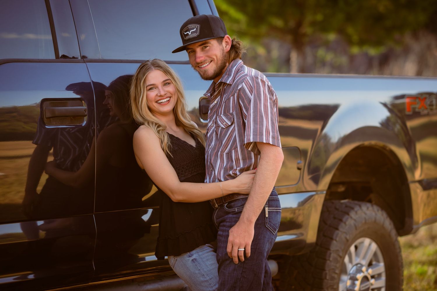 Happy couple embracing and smiling next to a black pickup truck outdoors.