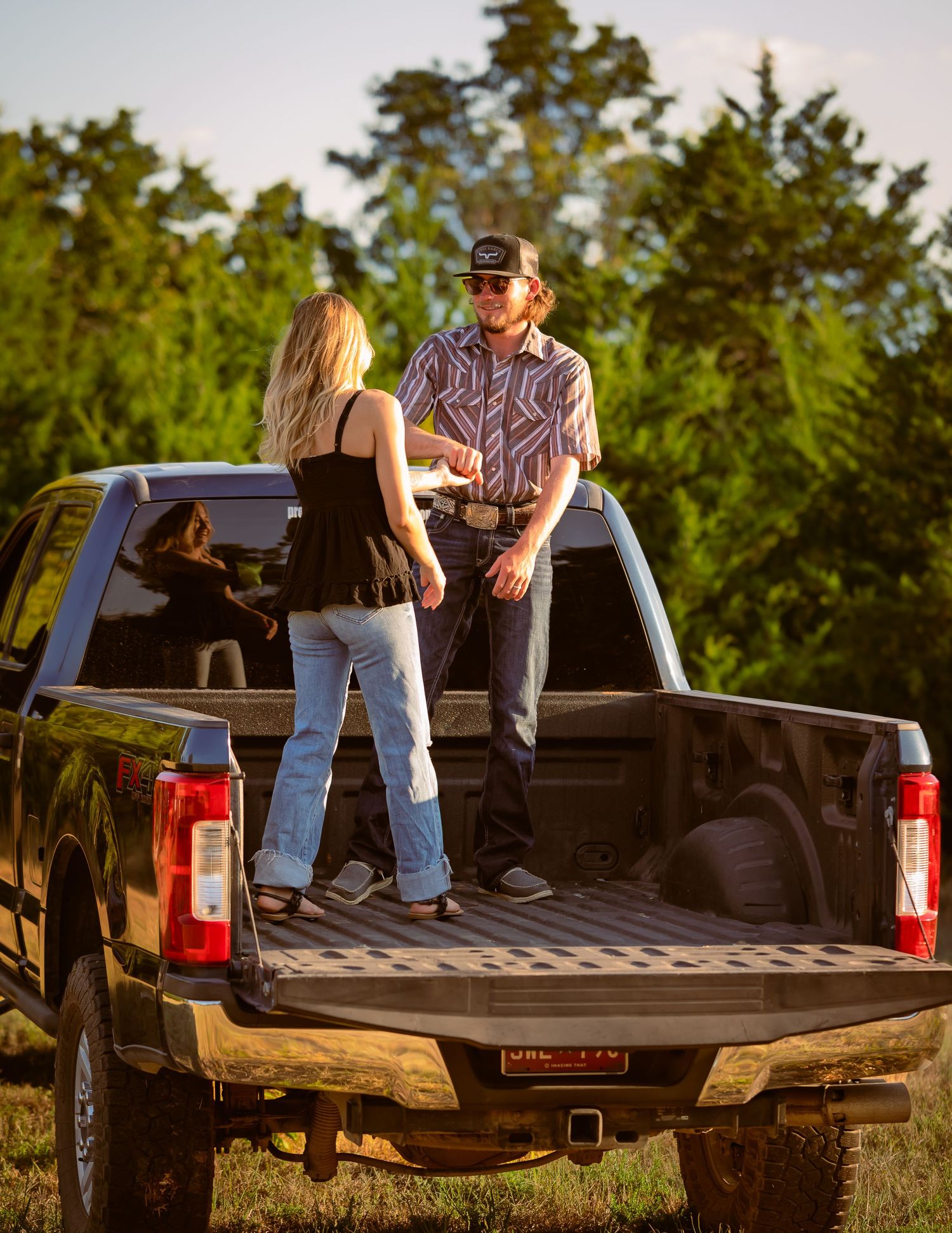 Young couple talking in the bed of a black Ford pickup truck in a green field.
