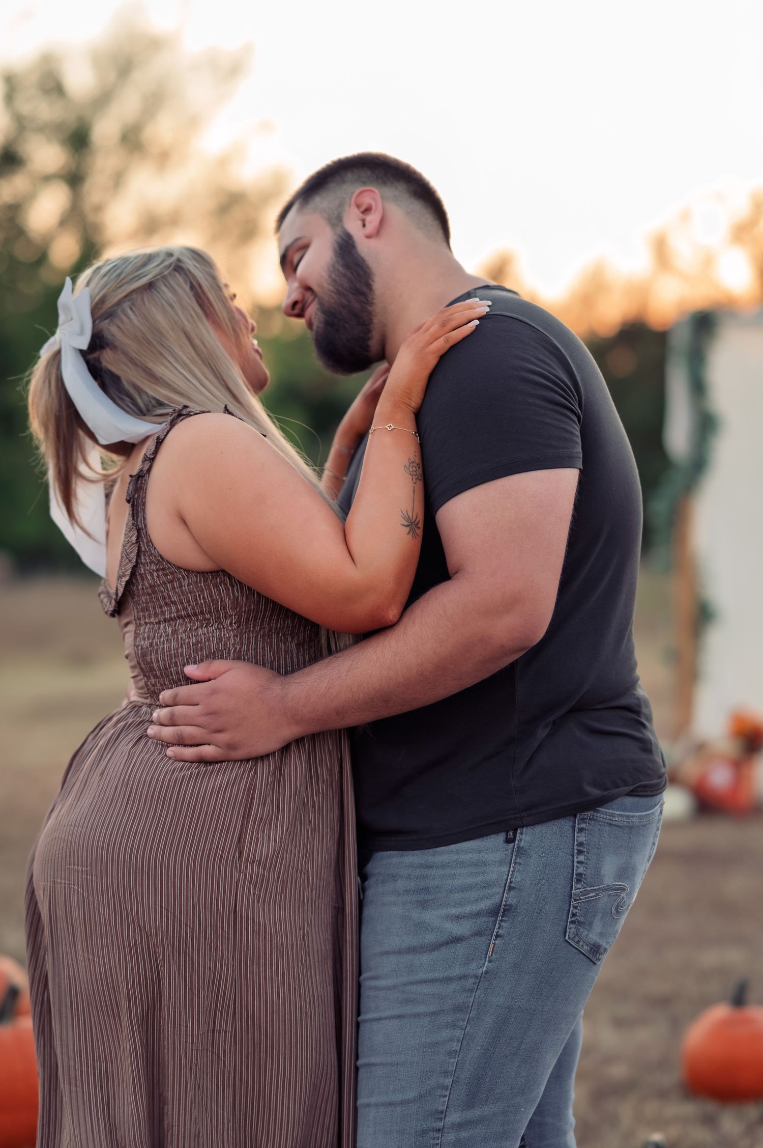 Couple embracing and about to kiss in pumpkin patch during warm fall engagement photo session.