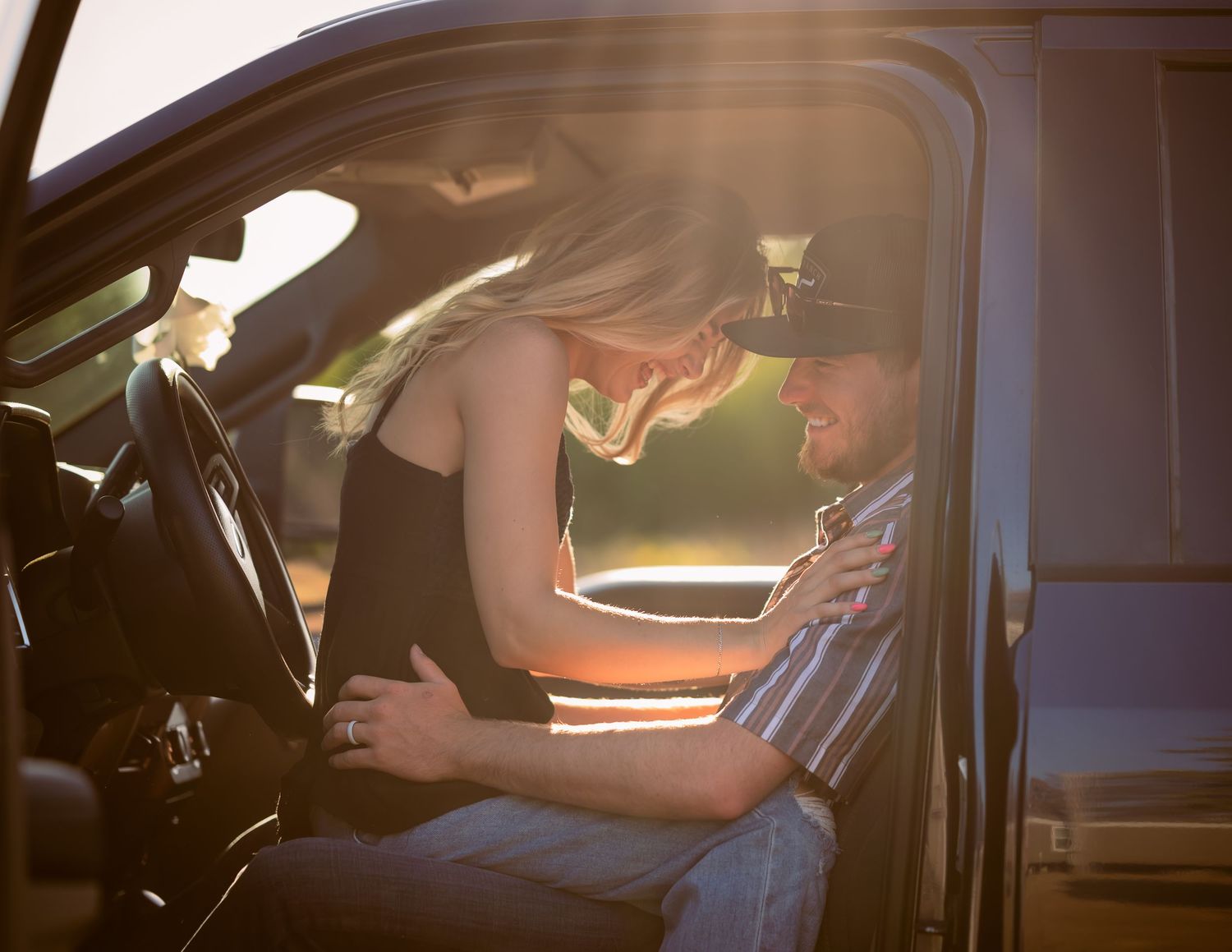 Couple sharing an intimate moment inside a truck cab at golden sunset.