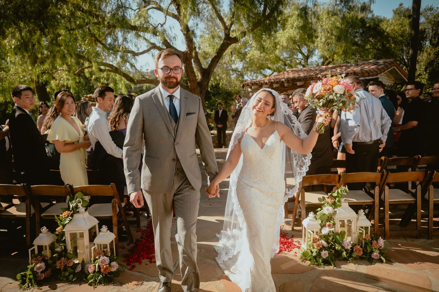 Smiling bride and groom walk hand-in-hand down the aisle after their outdoor wedding ceremony.