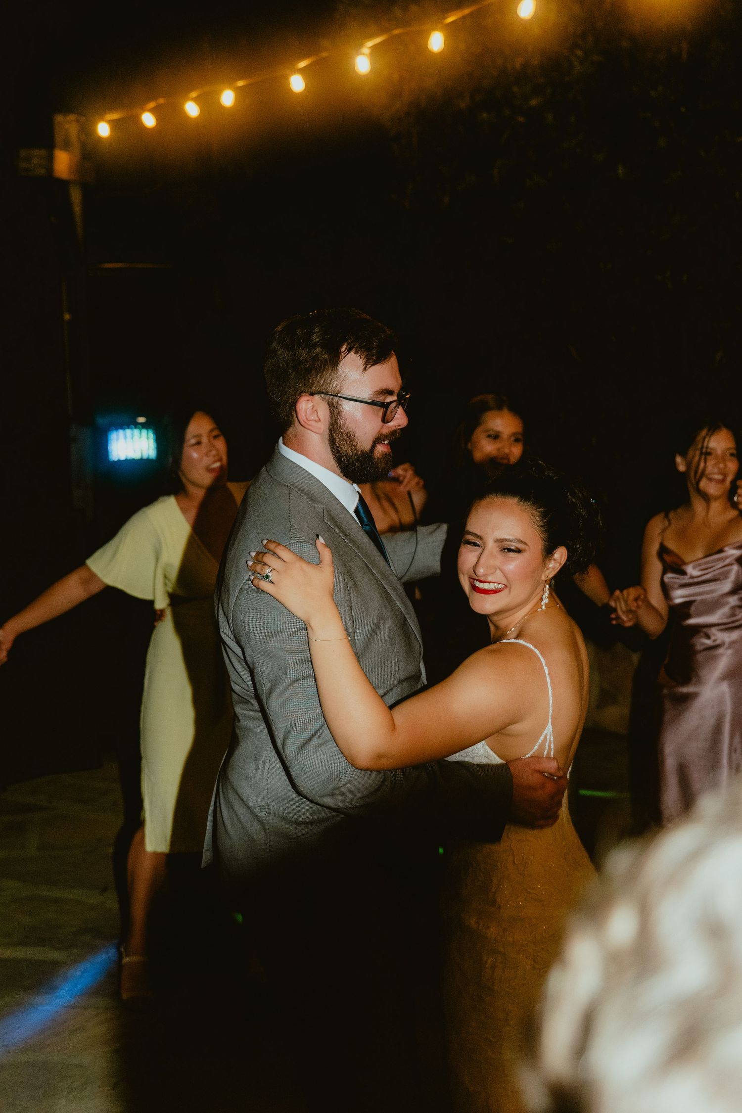 Smiling bride and groom dancing together at an outdoor evening wedding reception.
