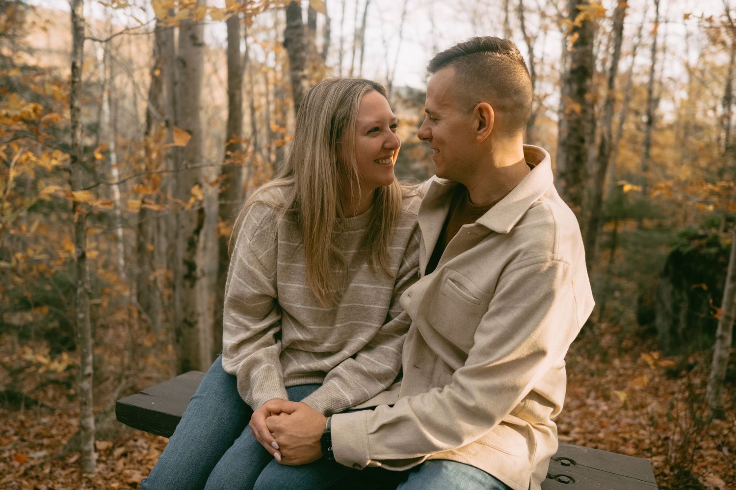 Smiling couple sitting closely together on a bench in a colorful autumn forest.
