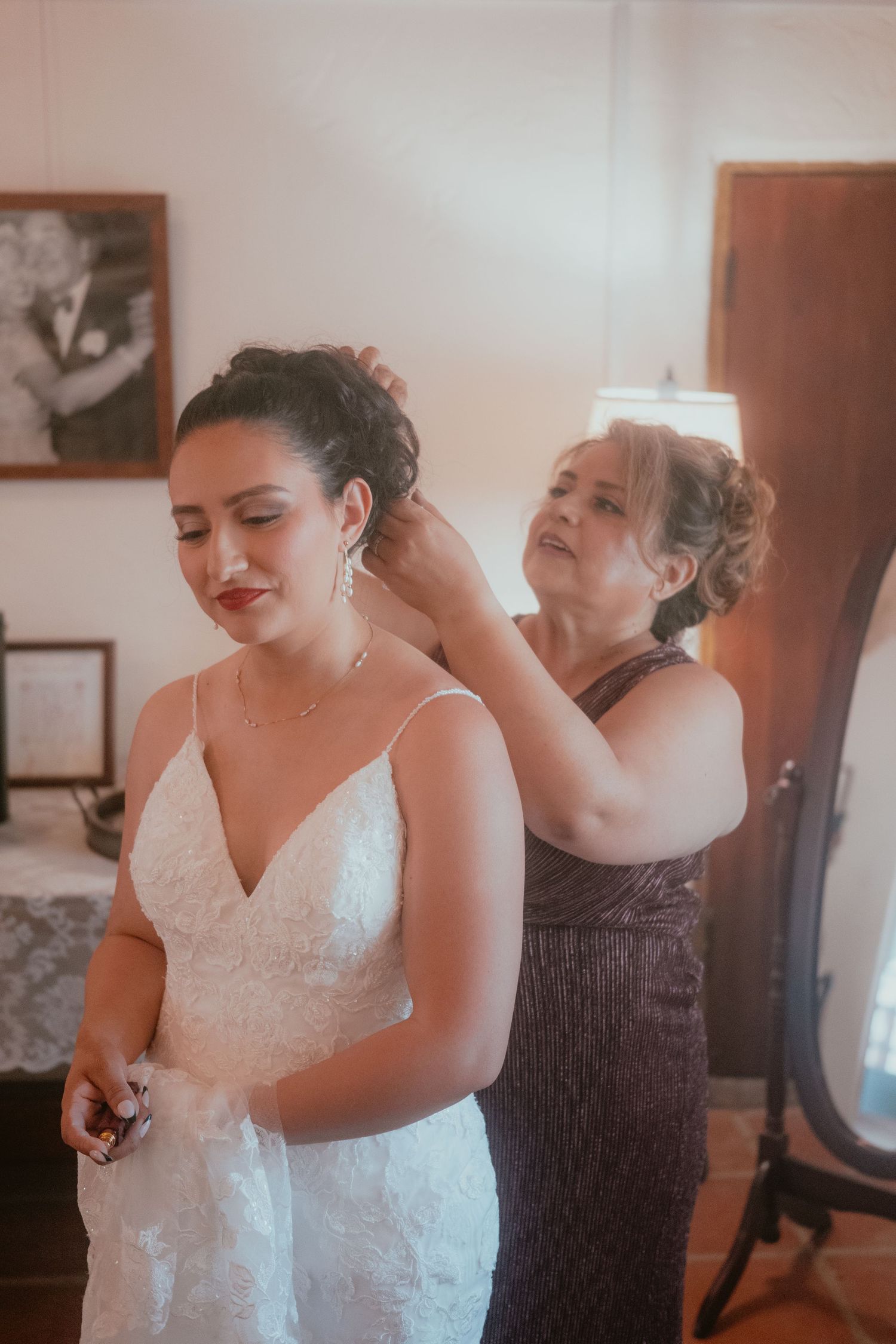 Mother helping bride with earrings while she wears a lace wedding gown before the ceremony.