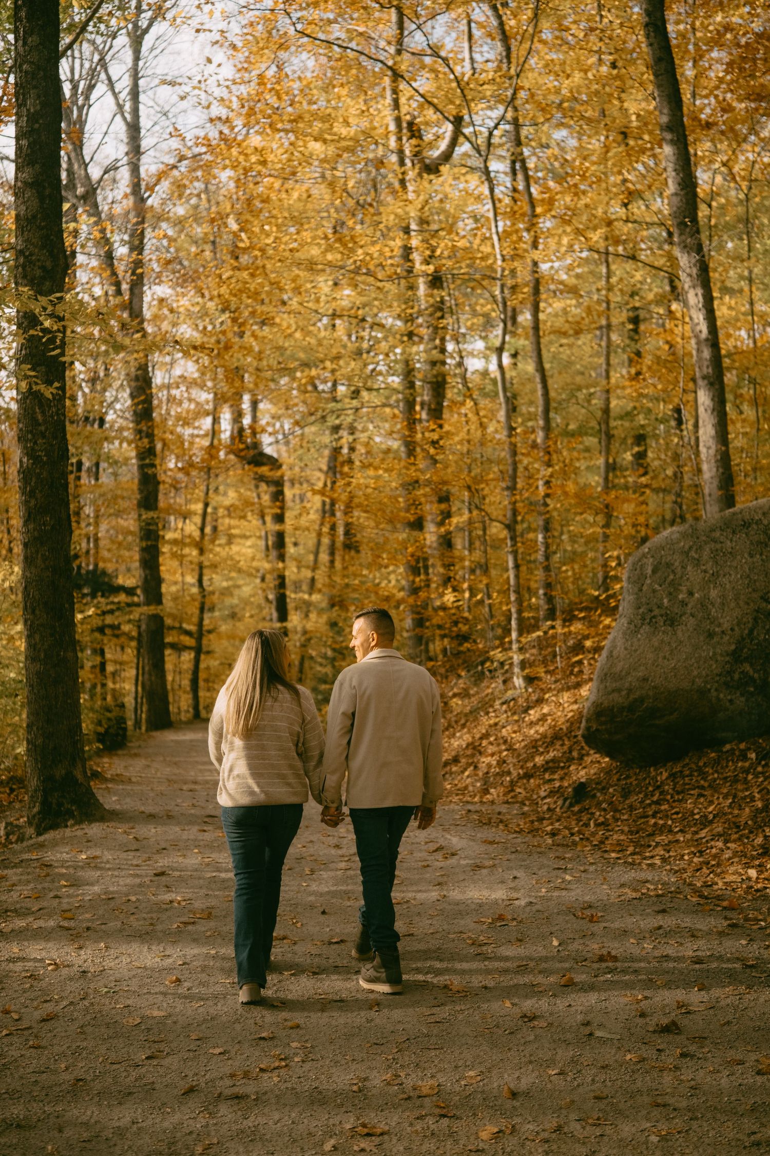 Couple walking hand in hand down a scenic autumn forest path with golden leaves.