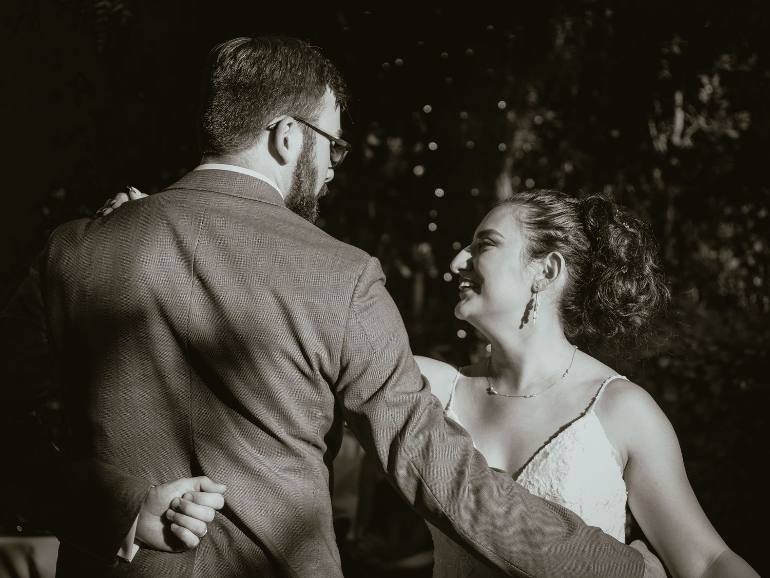 Black and white photo of bride laughing joyfully while dancing with groom at wedding.