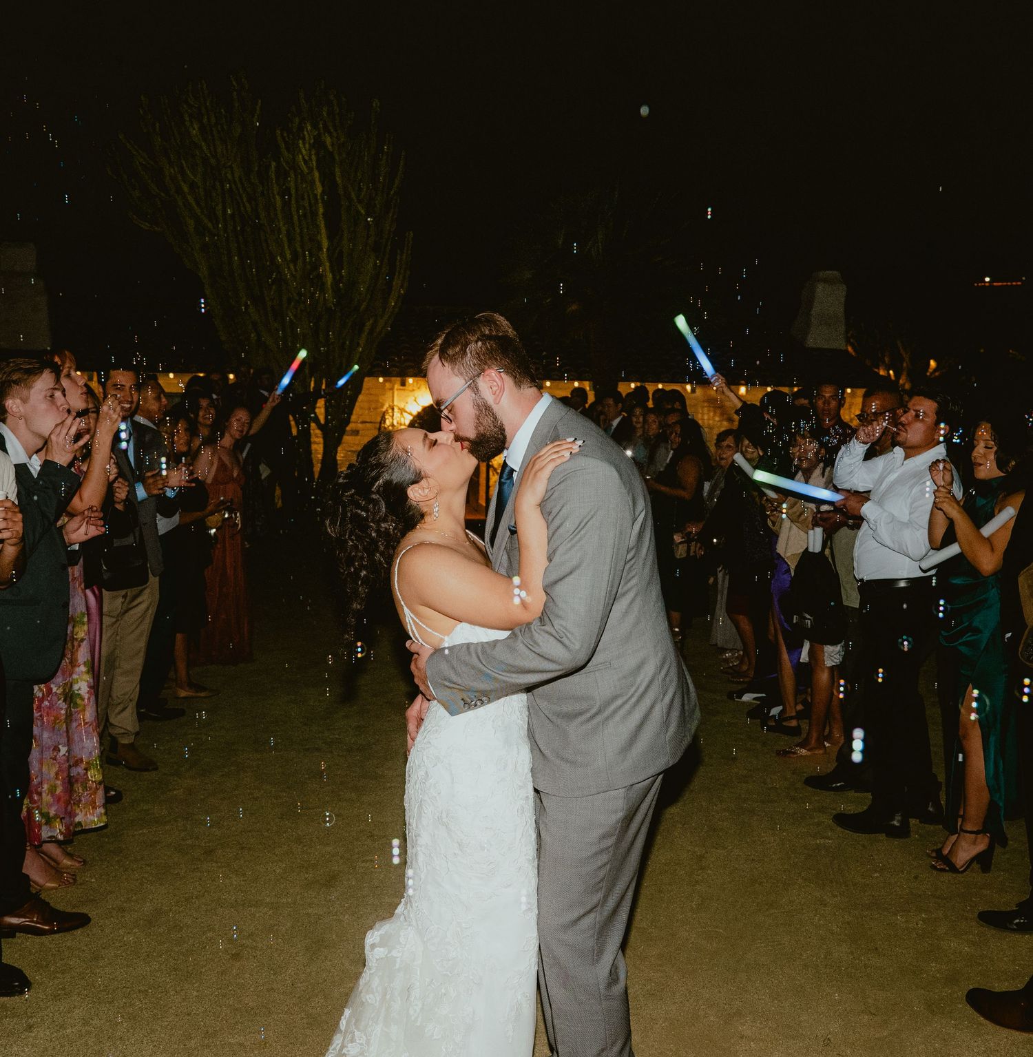Bride and groom share a kiss during a glow stick send-off at their outdoor wedding.