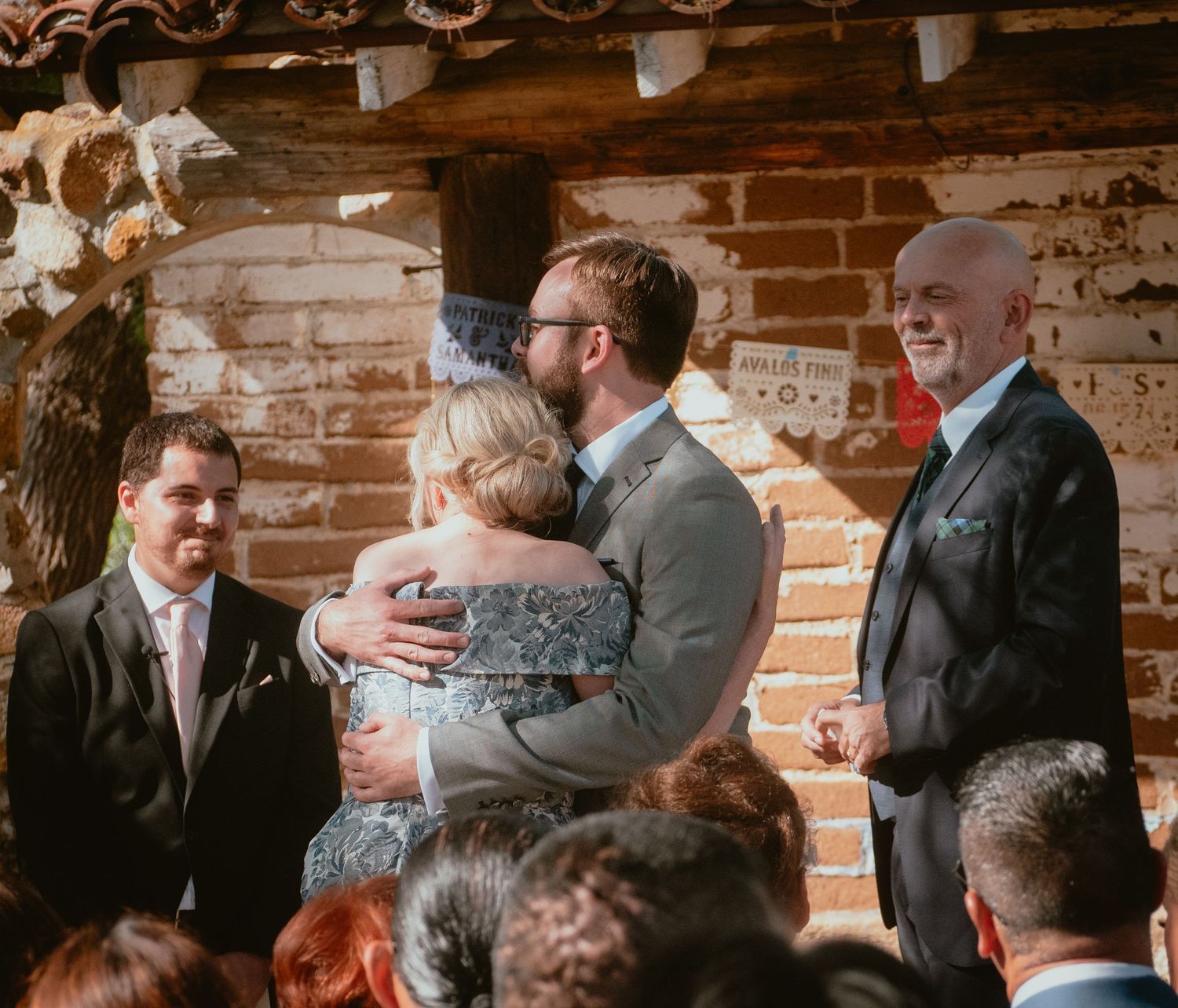 Groom embracing a guest during wedding ceremony inside rustic brick venue.