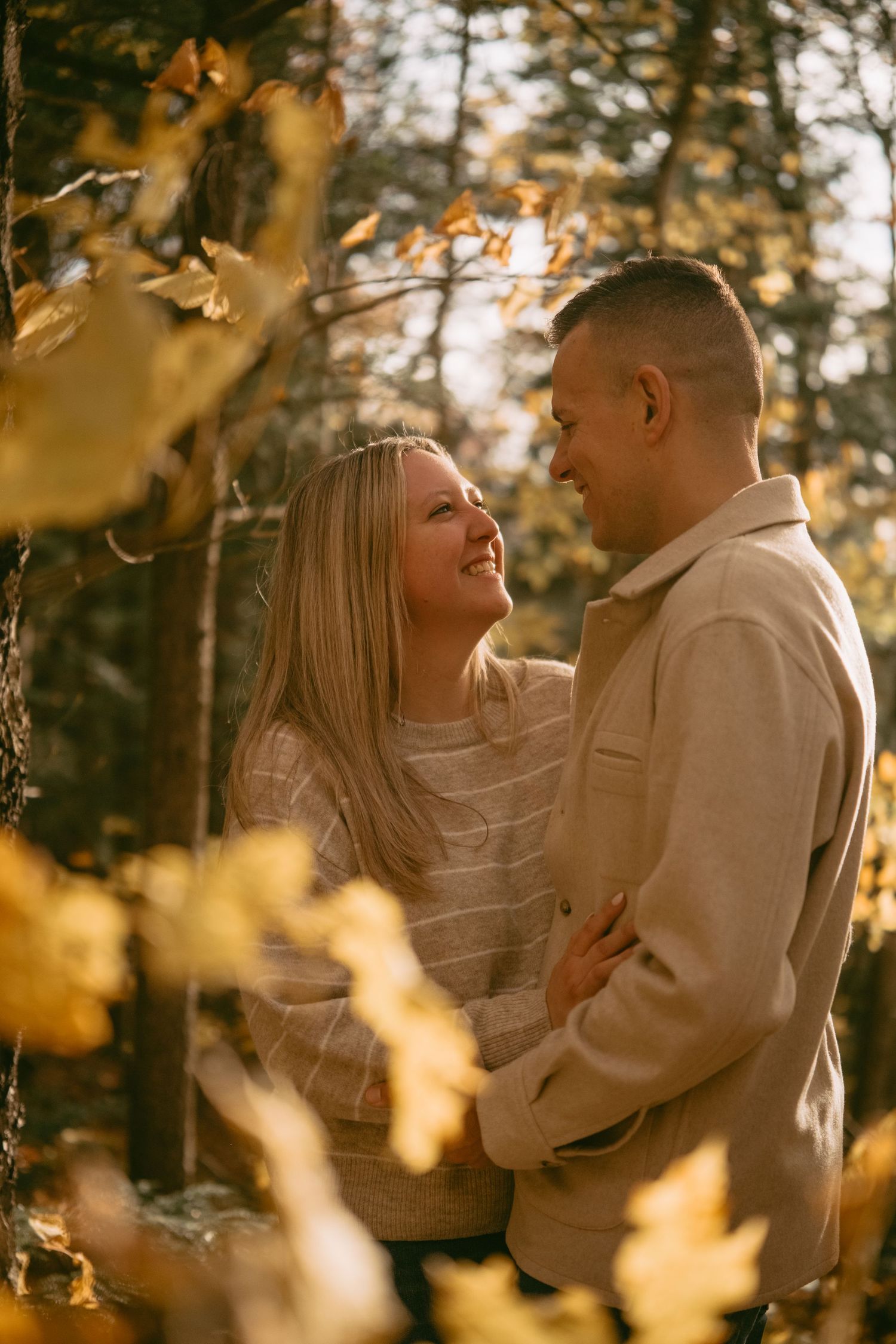 Smiling couple embracing in a glowing autumn forest with golden yellow foliage.