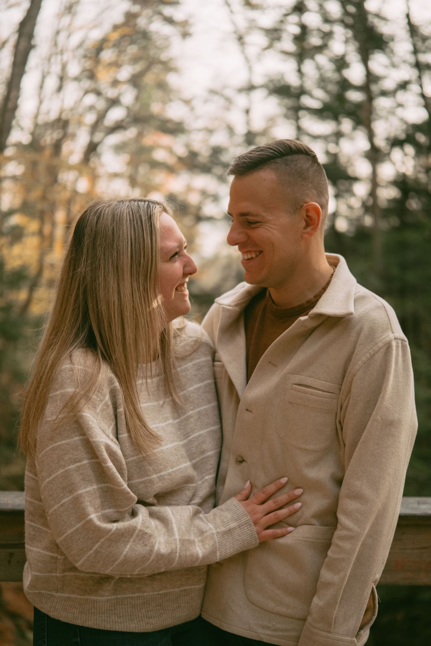 Joyful couple laughing together on a wooden bridge in an autumn forest setting.