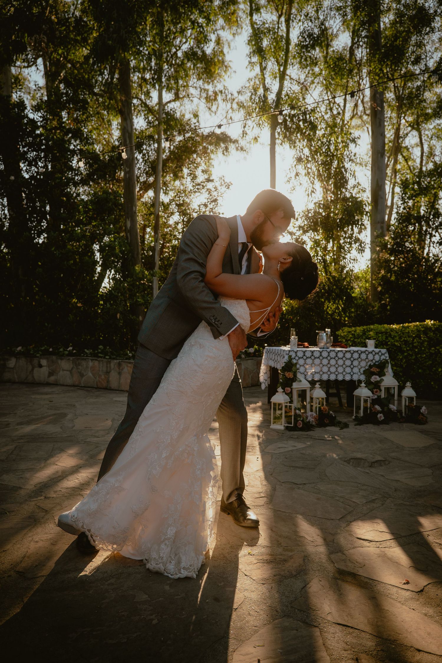 Bride and groom share a romantic dip kiss at golden hour during outdoor wedding reception.