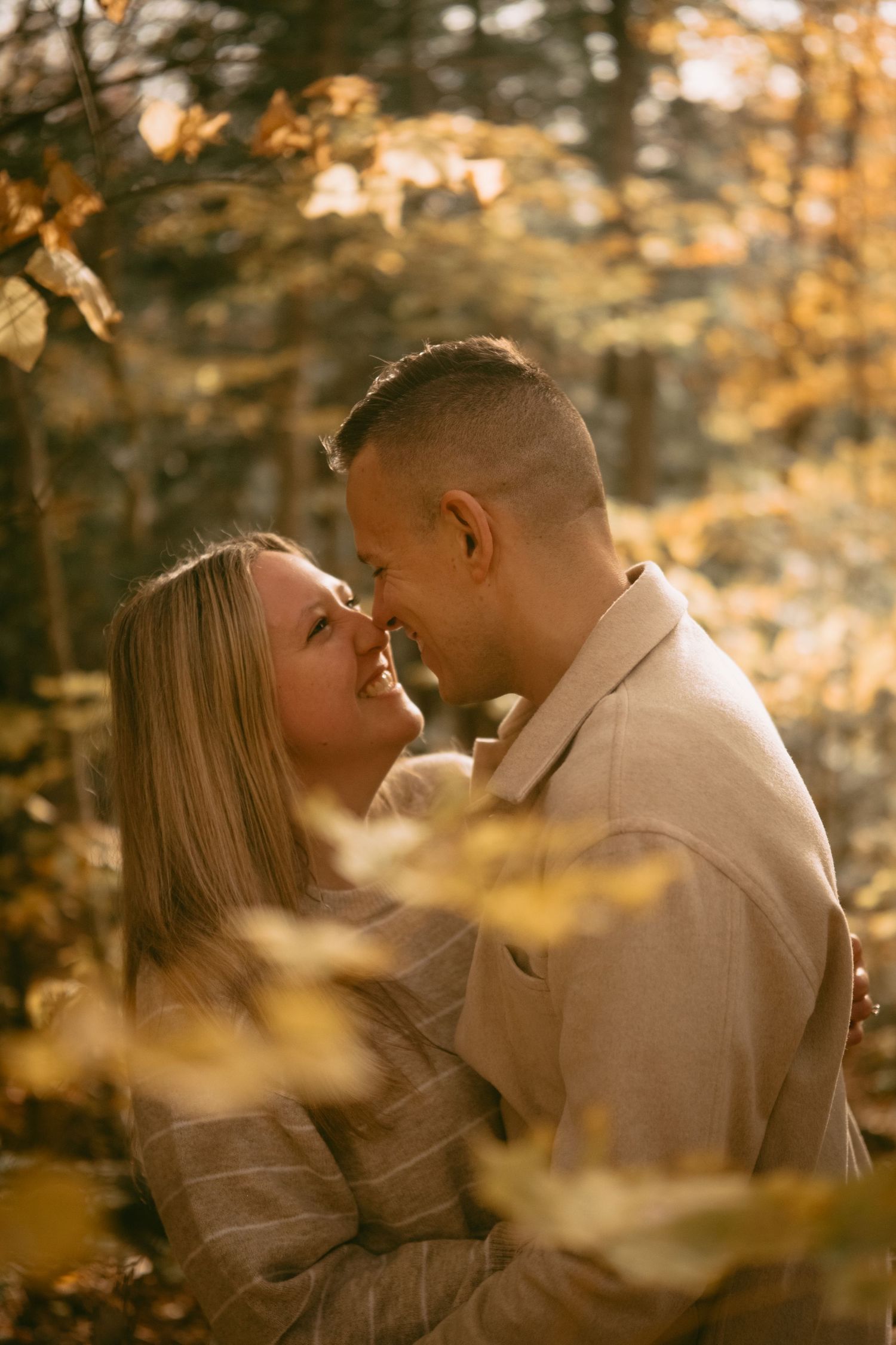 Romantic couple sharing an intimate moment nose-to-nose in a golden autumn forest.