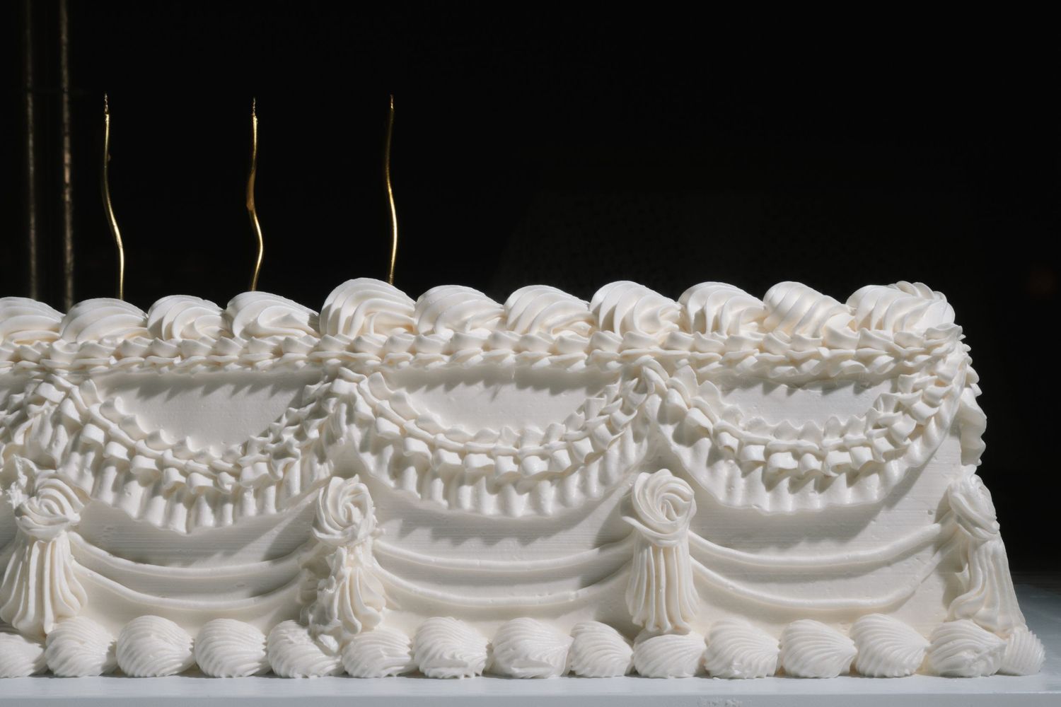 Elegant white wedding cake decorated with intricate royal icing swags and tassel details.