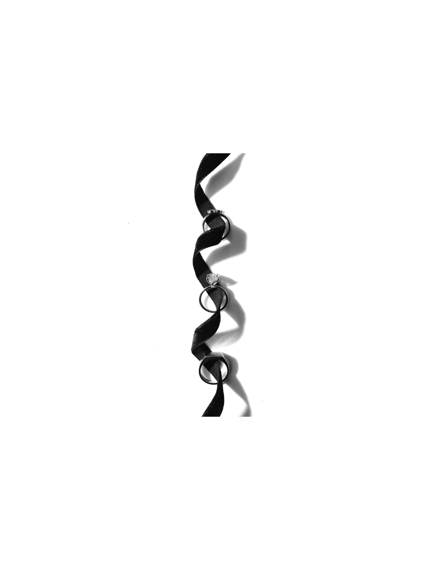 Minimalist black and white photo of a curling black ribbon with ring details on white background.