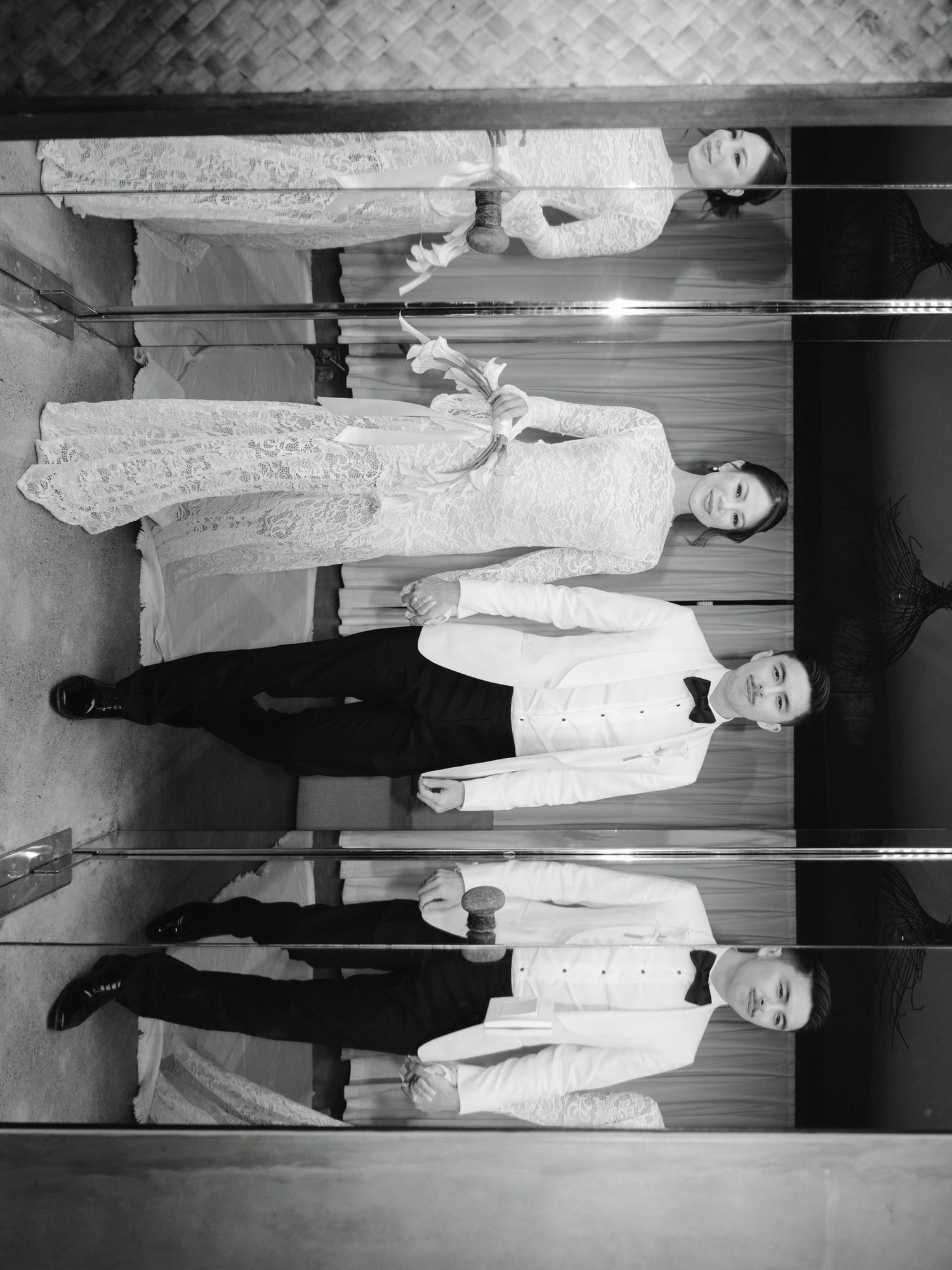 Black and white photo of wedding party reflected in mirrors wearing formal attire.