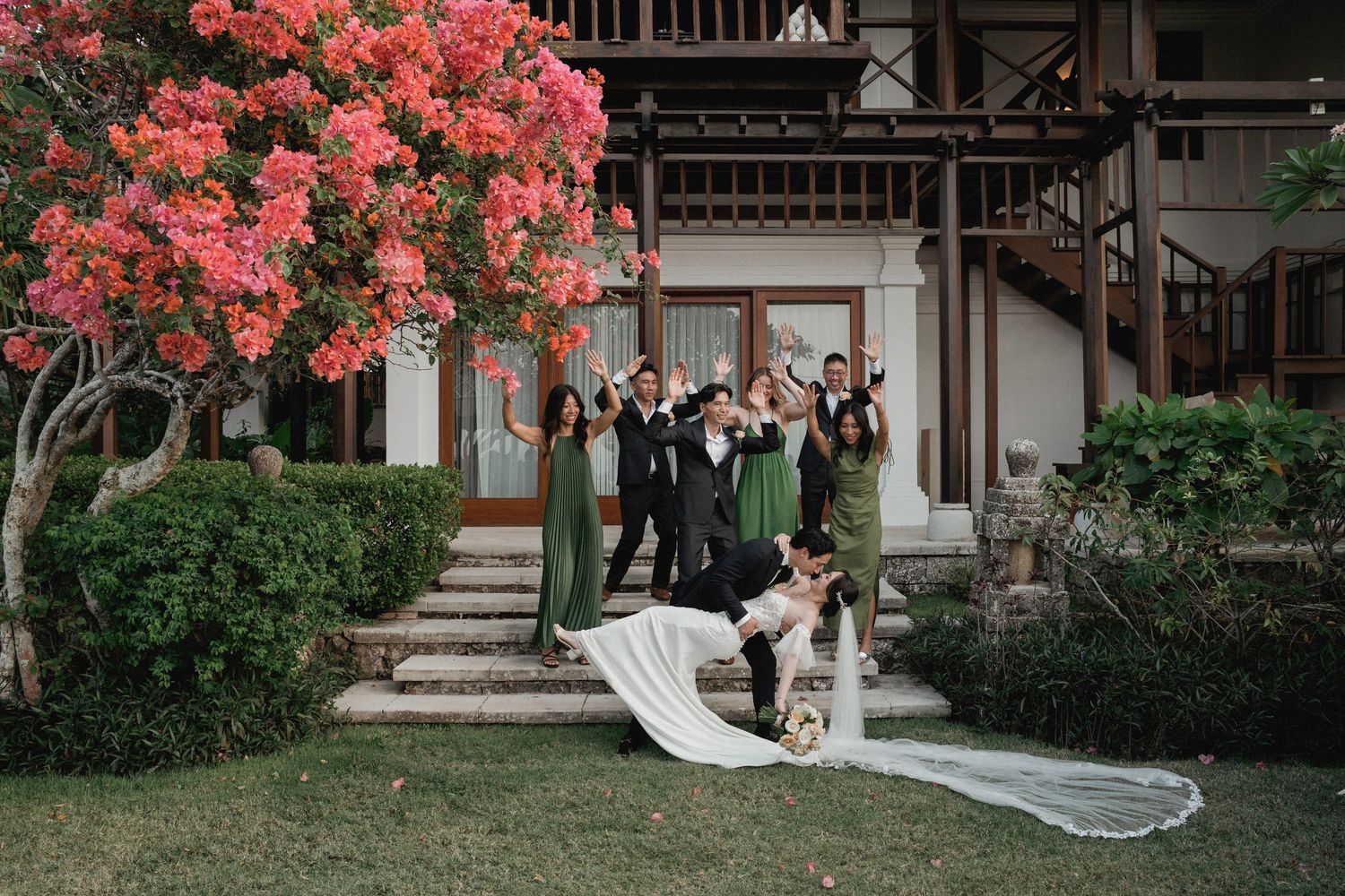 Wedding party poses on steps with blooming bougainvillea and flowing bridal veil.