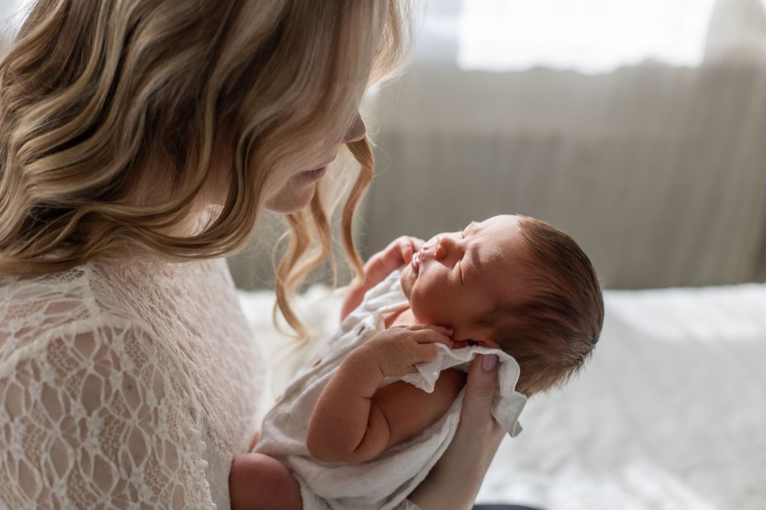 Tender moment of a mother with wavy hair gently holding and gazing at her newborn baby.
