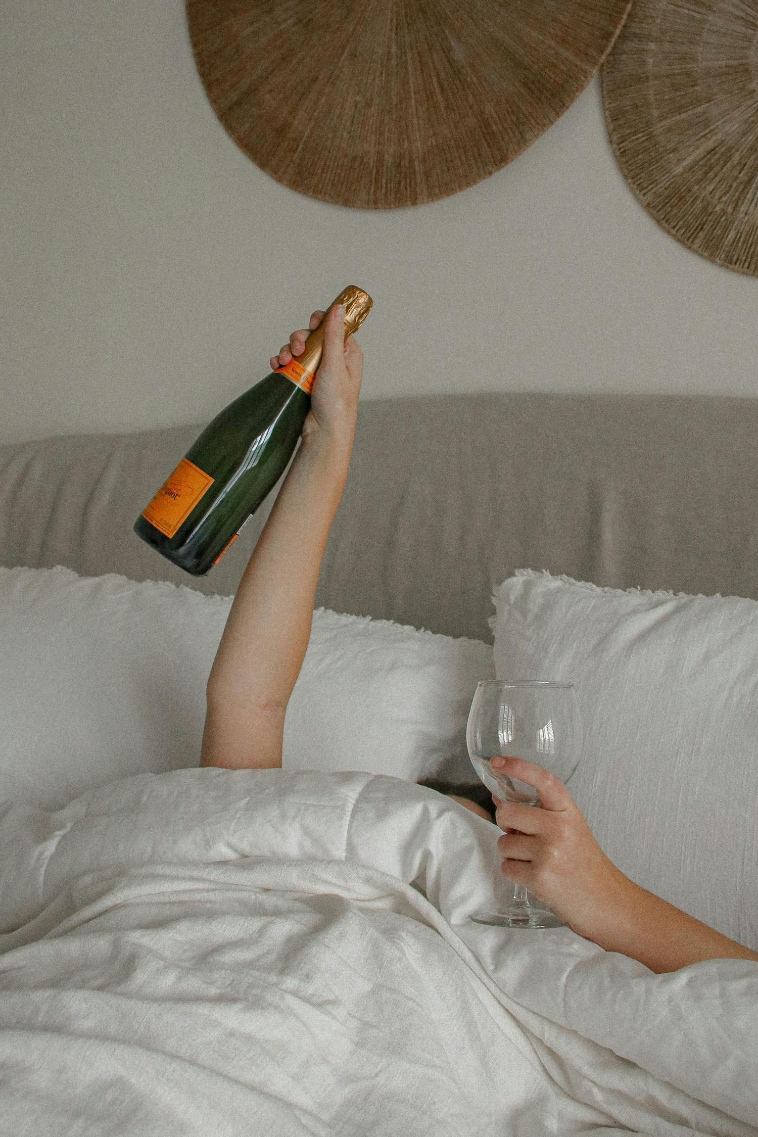 Artistic photo of champagne bottle and wine glass against neutral background with woven wall decor.