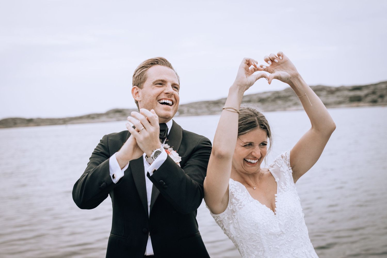 Newlywed couple celebrates joyfully by the water on their wedding day.