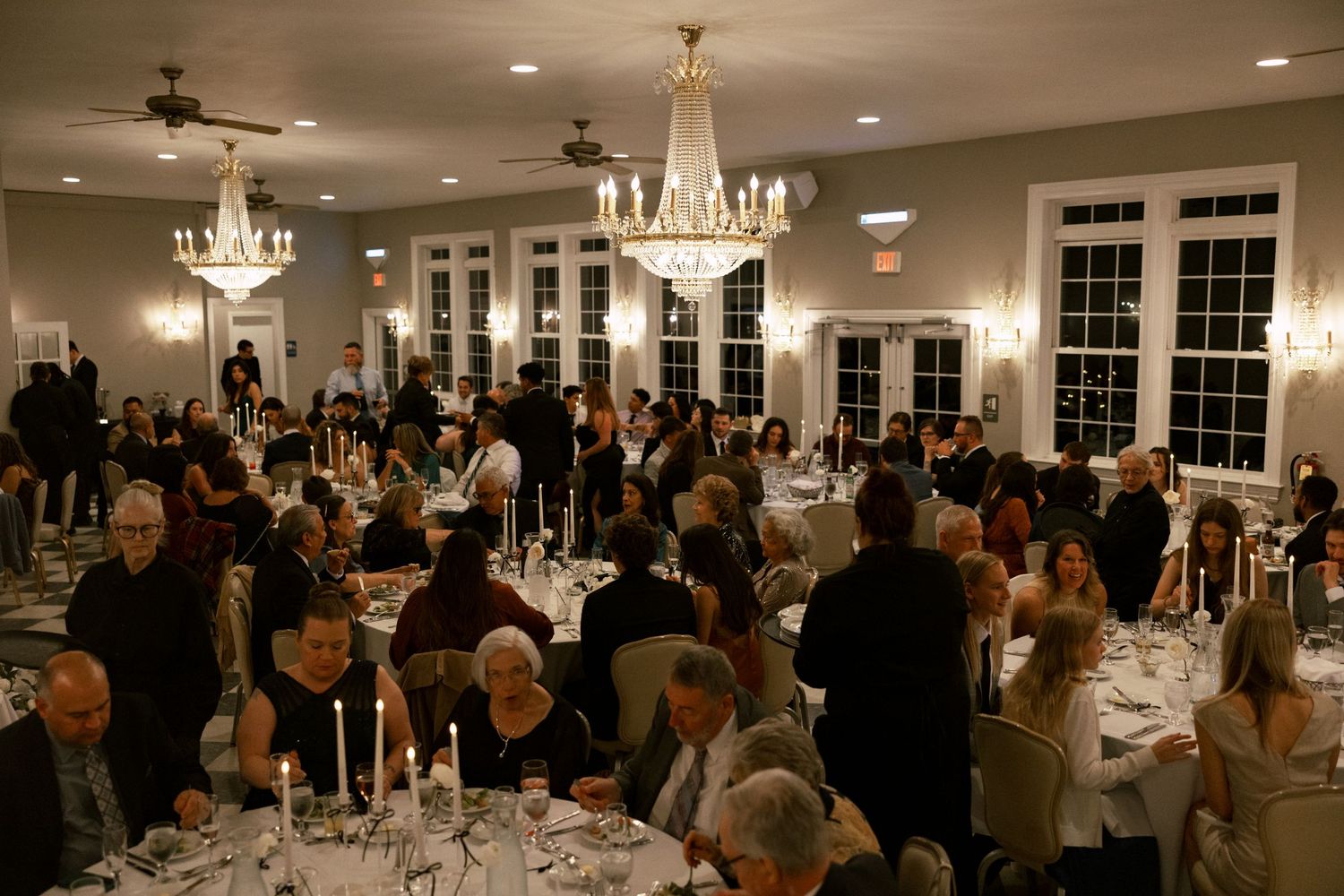 An elegant reception hall filled with guests, chandeliers, and dining tables.