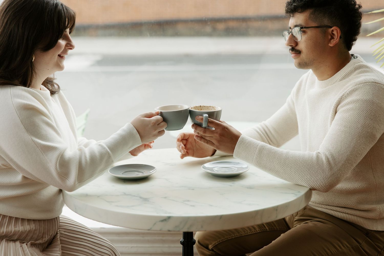 Two people in white sweaters share coffee at a round table during an intimate moment.