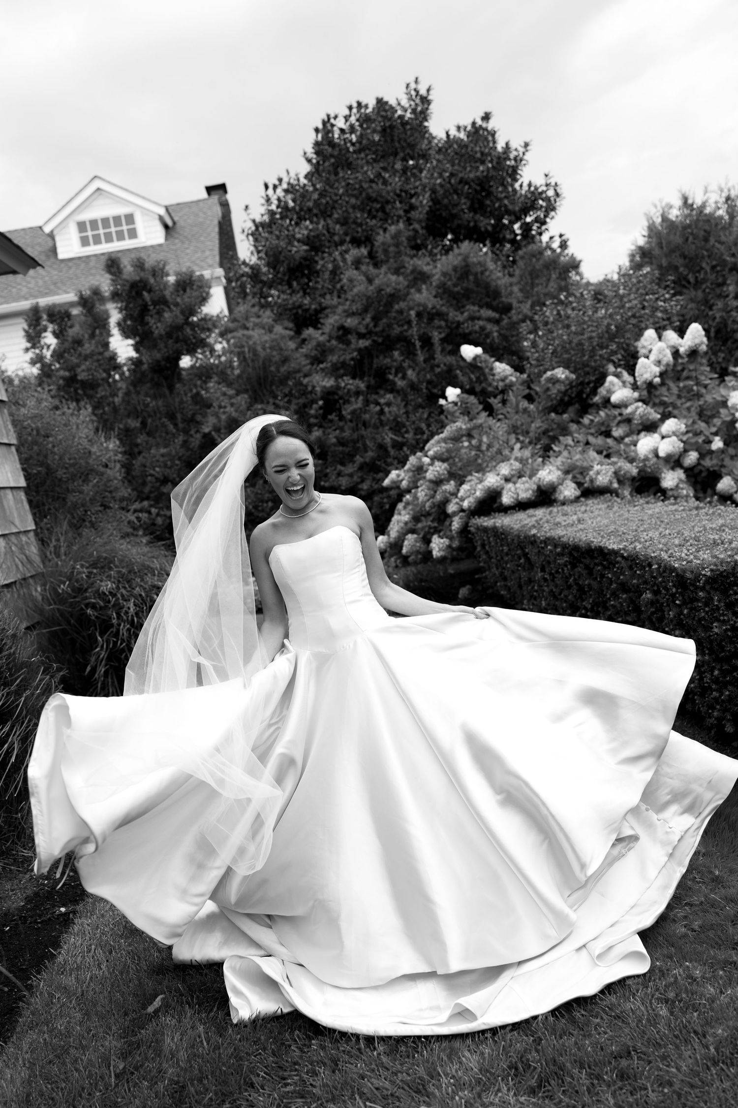 A bride in a flowing white wedding dress twirls gracefully on a grassy lawn, creating a circular motion with the fabric.