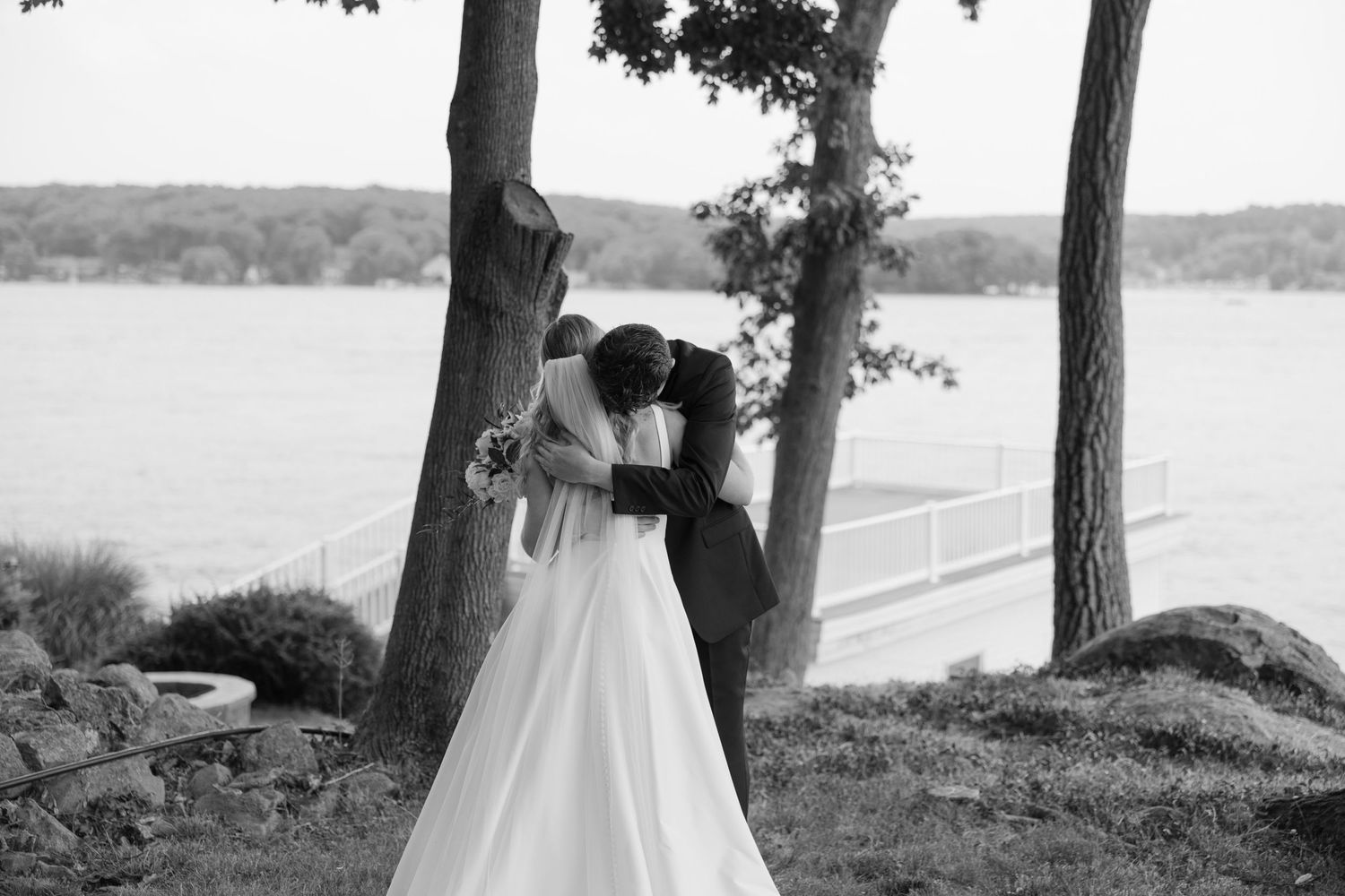 A couple shares a romantic moment by a lake surrounded by pine trees.