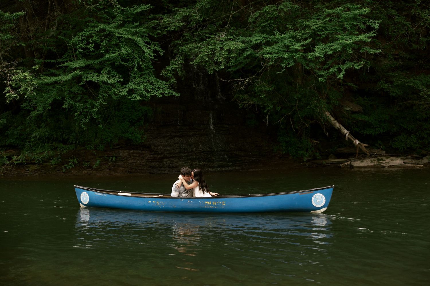 A blue canoe floating on calm waters surrounded by dense forest.
