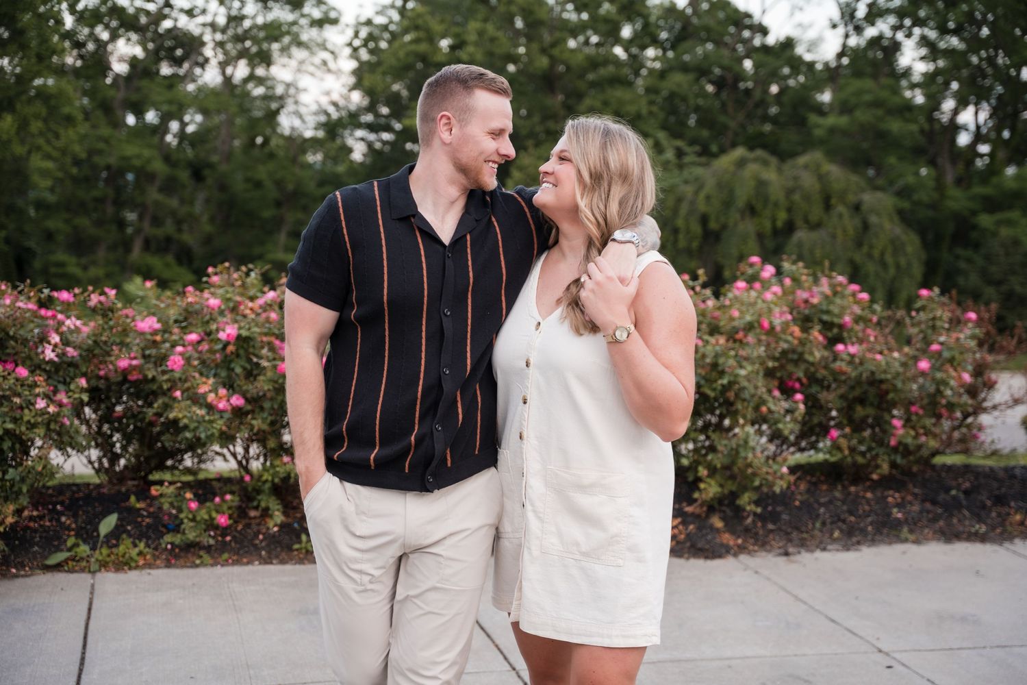 A couple shares intimate moments together in a garden setting surrounded by blooming pink roses.