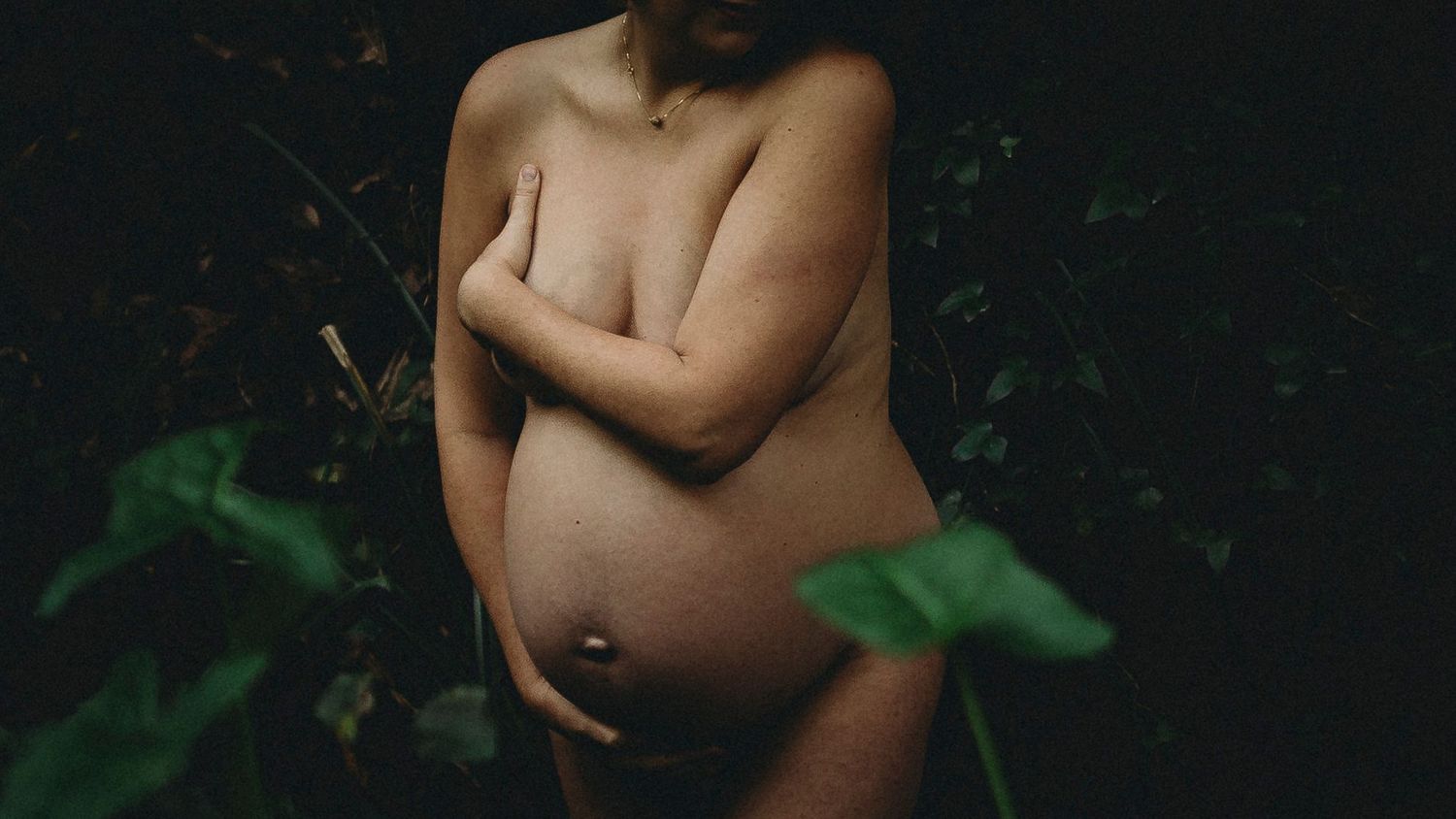 foto preto e colorida  grávida Nua na natureza com mãos na barriga durante sessão fotográfica de grávida em Caldas Da Rainha