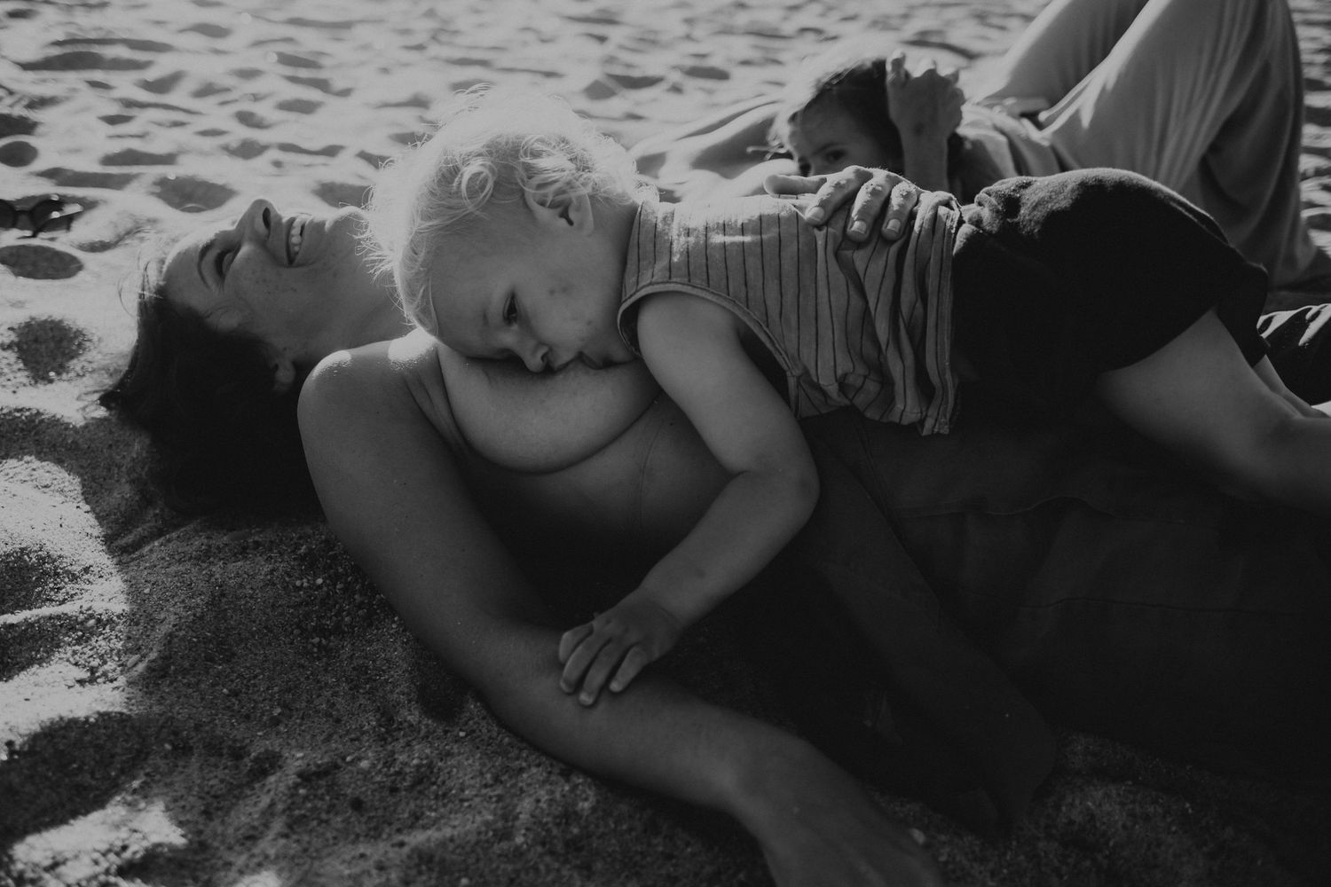 foto preto e branco de mãe na praia deitada na areia a amamentar o bébé em Peniche Portugal
