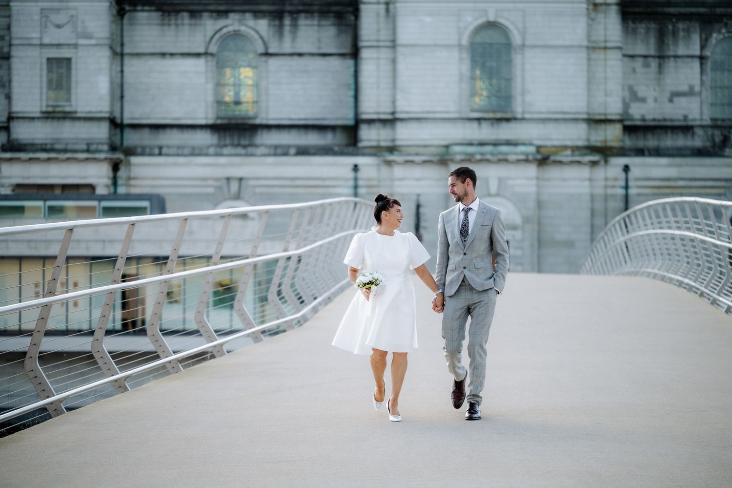 Bride and groom walking hand in hand on a modern bridge in Athlone, Ireland.