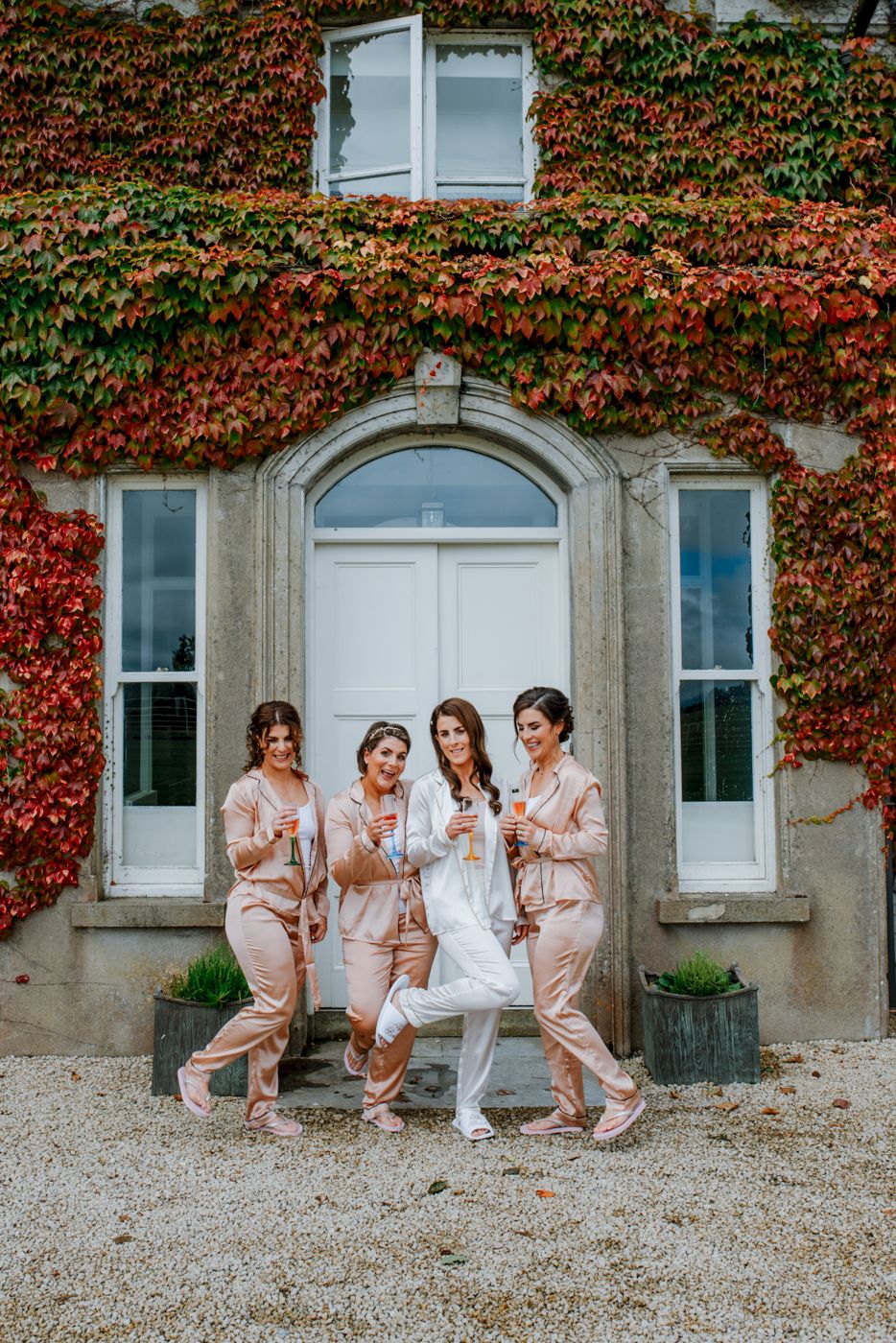 Bride with bridesmaids in matching satin outfits celebrating before the wedding at a country house in Ireland.
