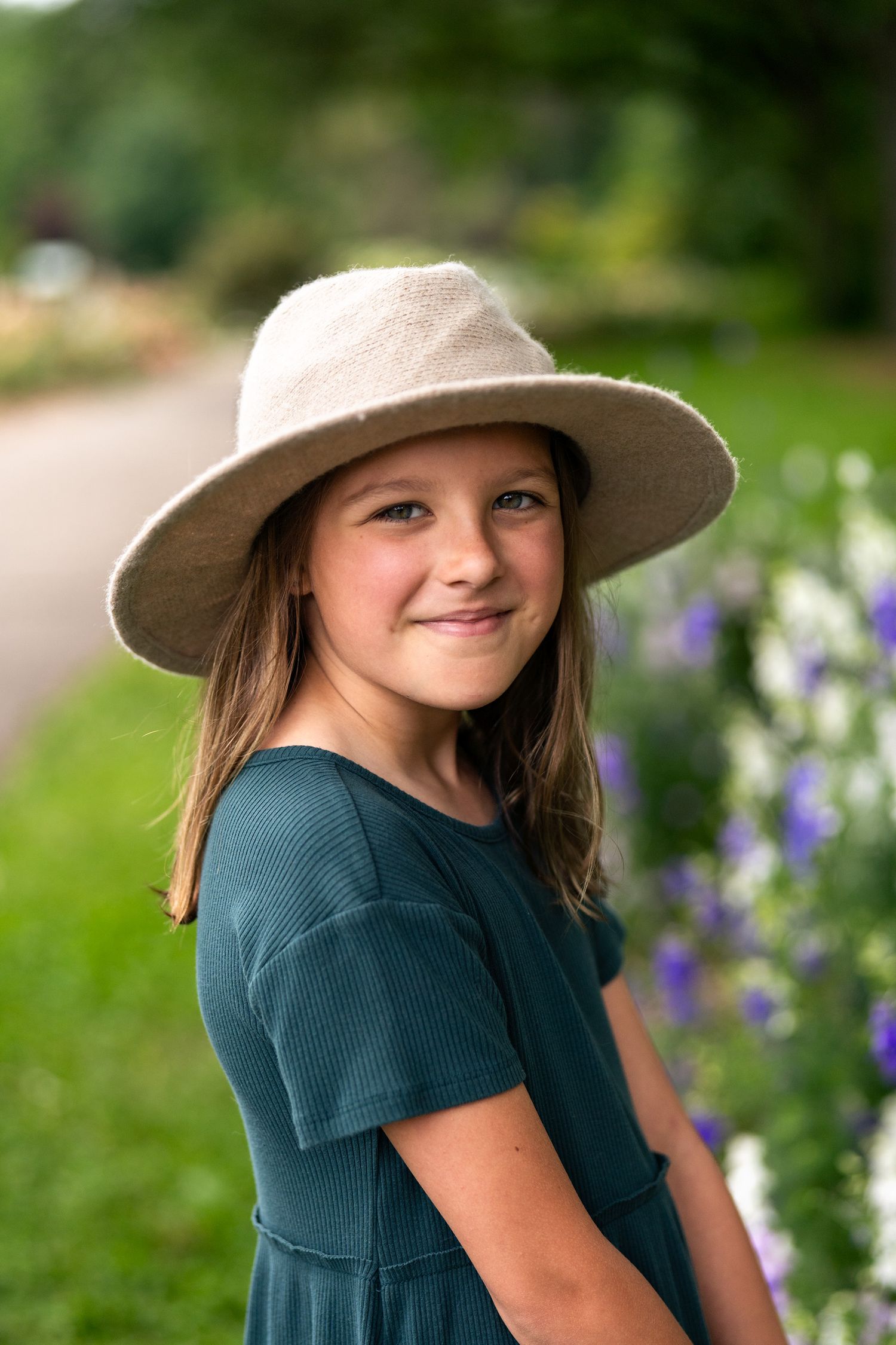 Smiling senior girl wearing a wide-brim hat surrounded by summer flowers during an outdoor senior portrait session in Columbus, Ohio by Jami