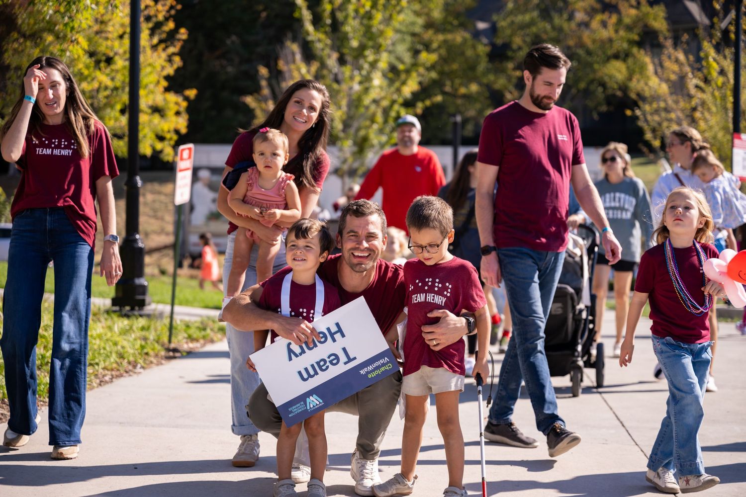 Students in maroon shirts walk together during a campus event on a sunny day.
