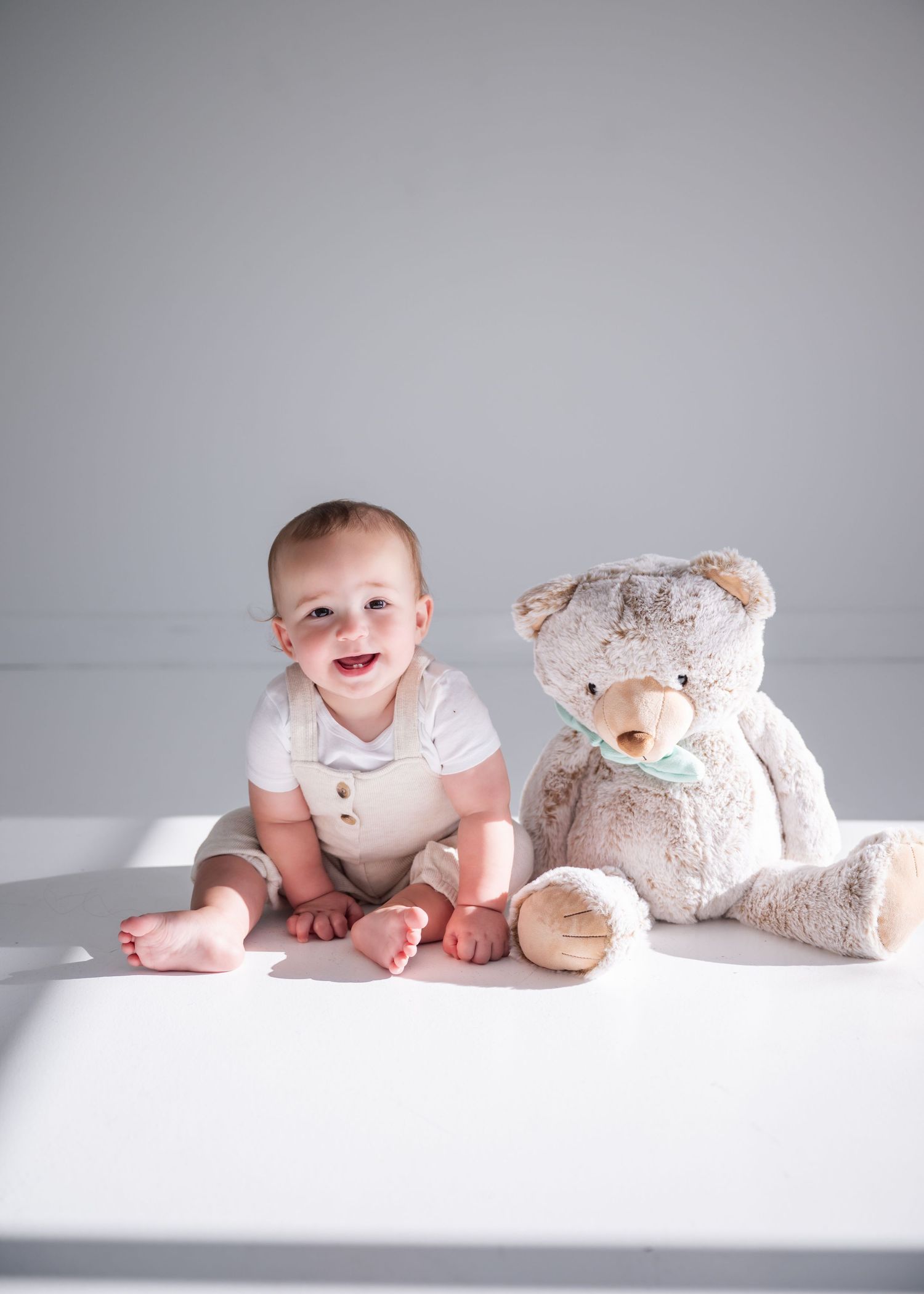A baby and teddy bear sitting together in a minimalist white setting shown in four progressive poses.
