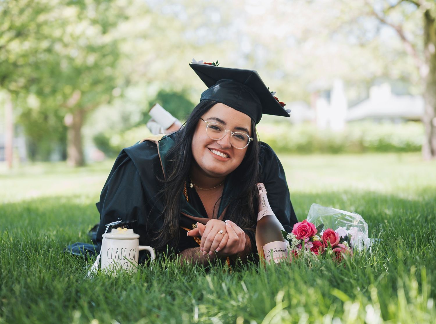 Graduation session lying on grass with flowers and champagne celebrating her graduation.