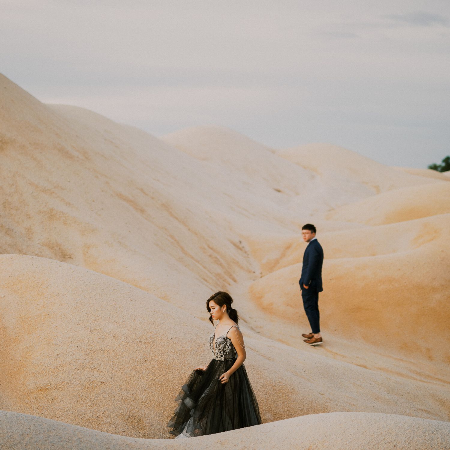 Artistic desert photoshoot featuring smooth sand dunes under cloudy sky.