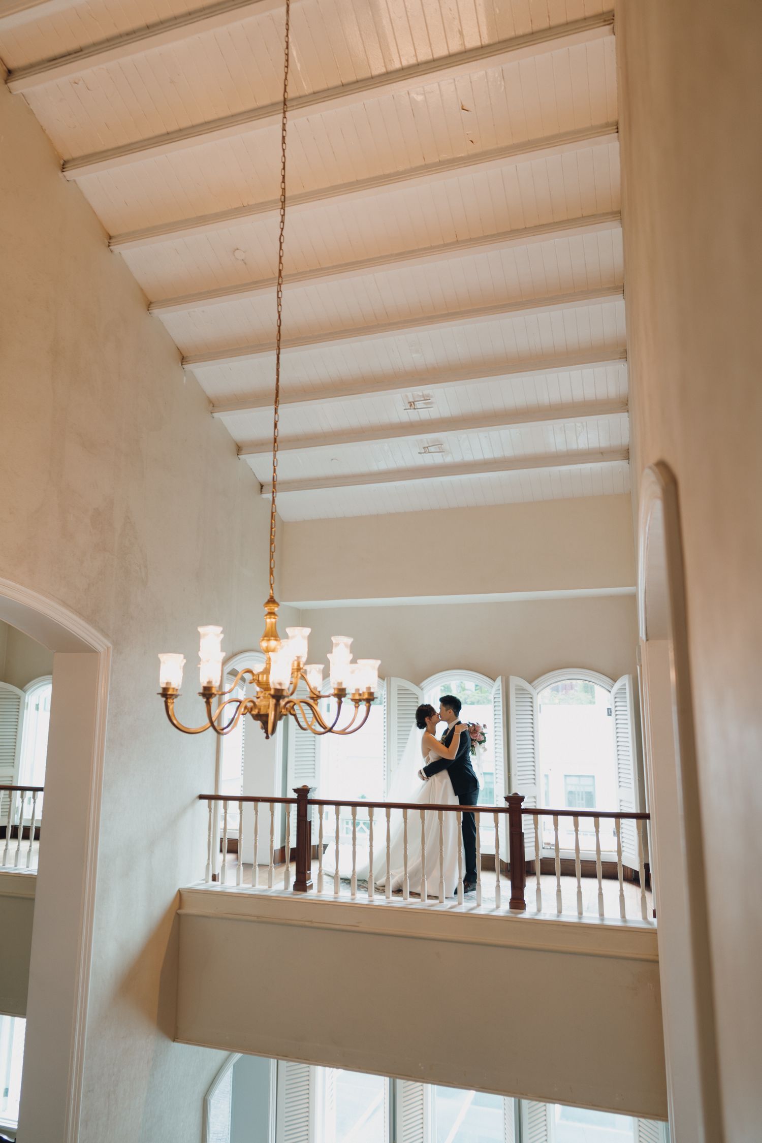Couple embracing on elegant balcony with chandelier in grand venue.