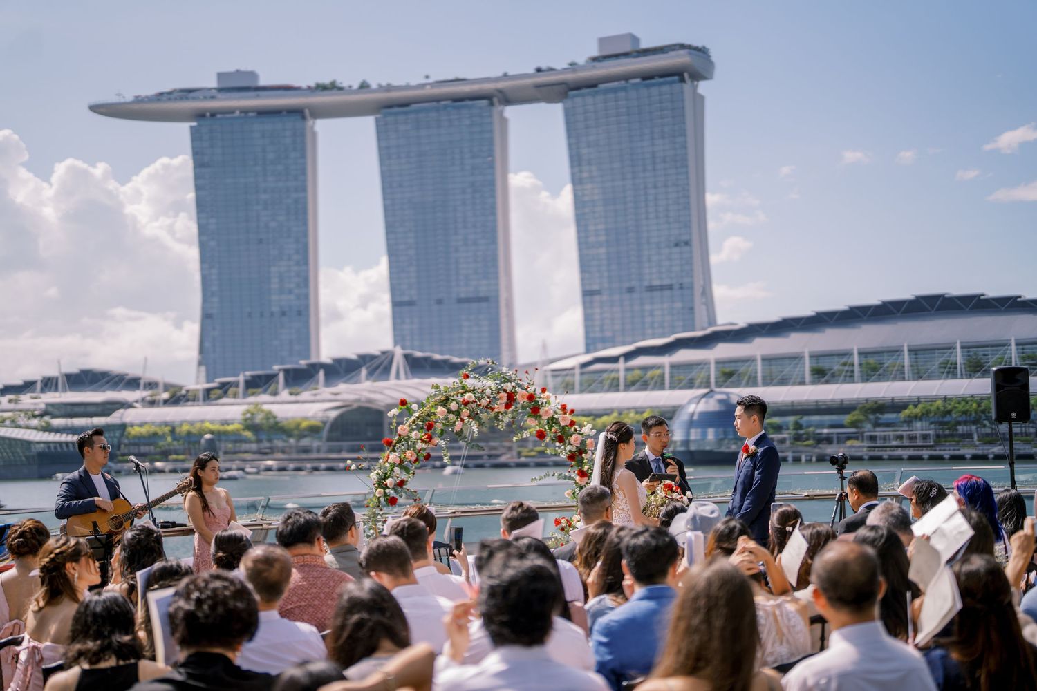 Wedding guests taking photos of celebration with Marina Bay Sands visible in background.